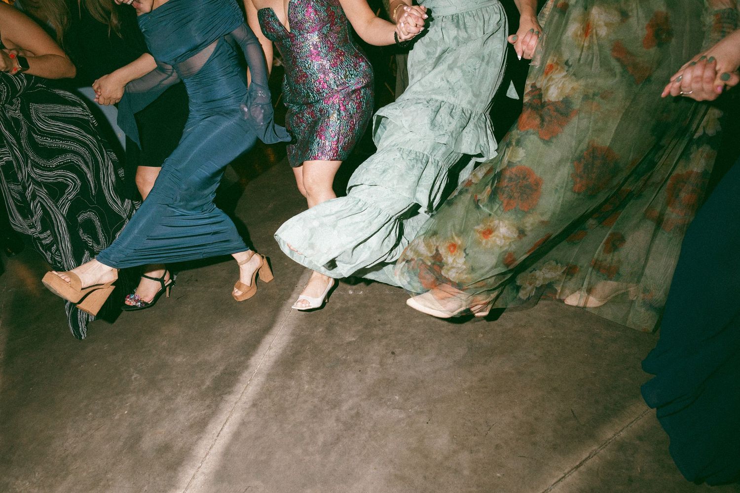 Group of women dancing in colorful dresses and heels on a concrete floor at a party or event.