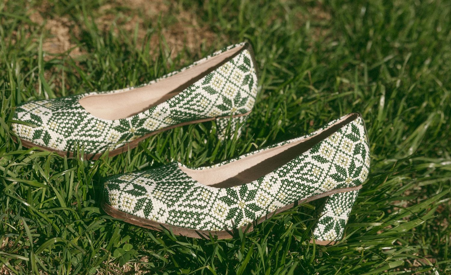 Green and white patterned low-heel bridal shoes with floral design resting on lush green grass.