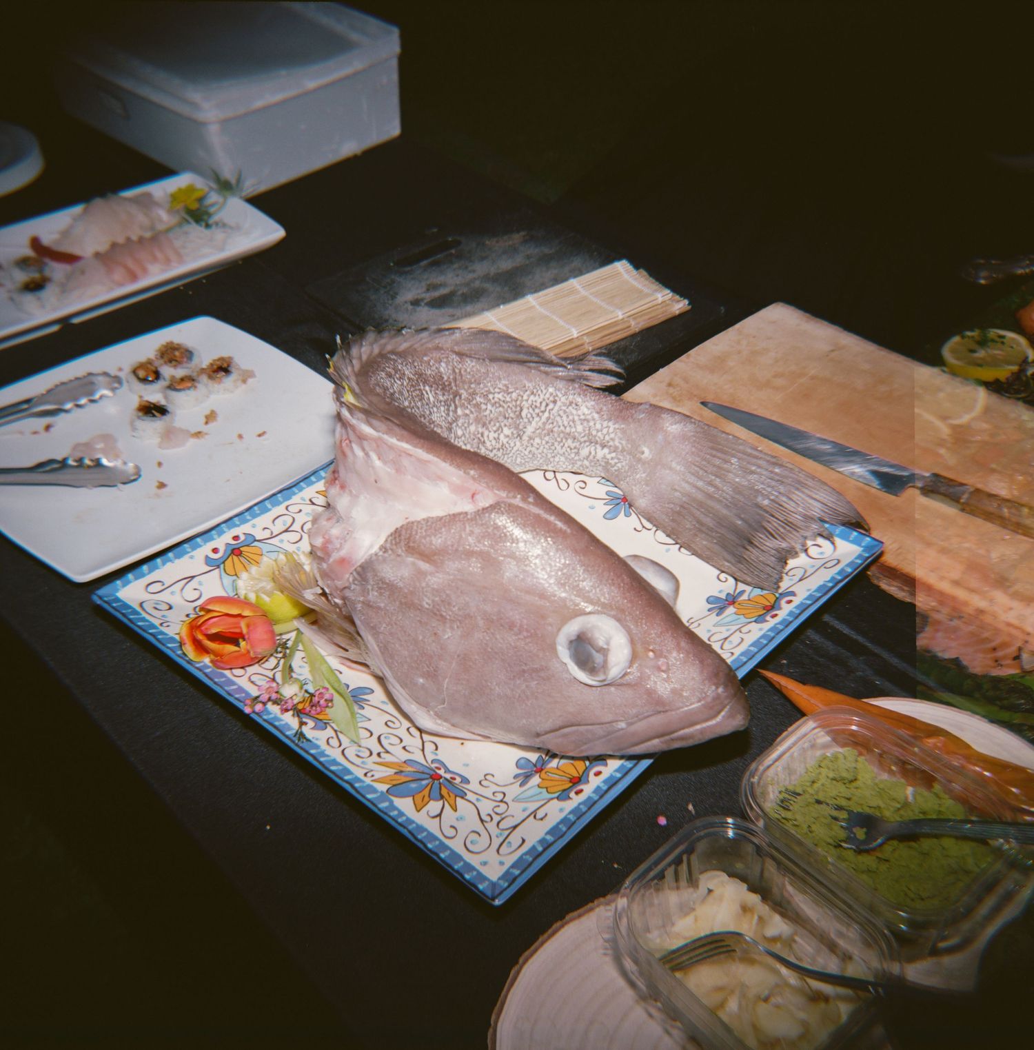 Fresh whole fish displayed on a decorative plate surrounded by food preparation items on a dark table.