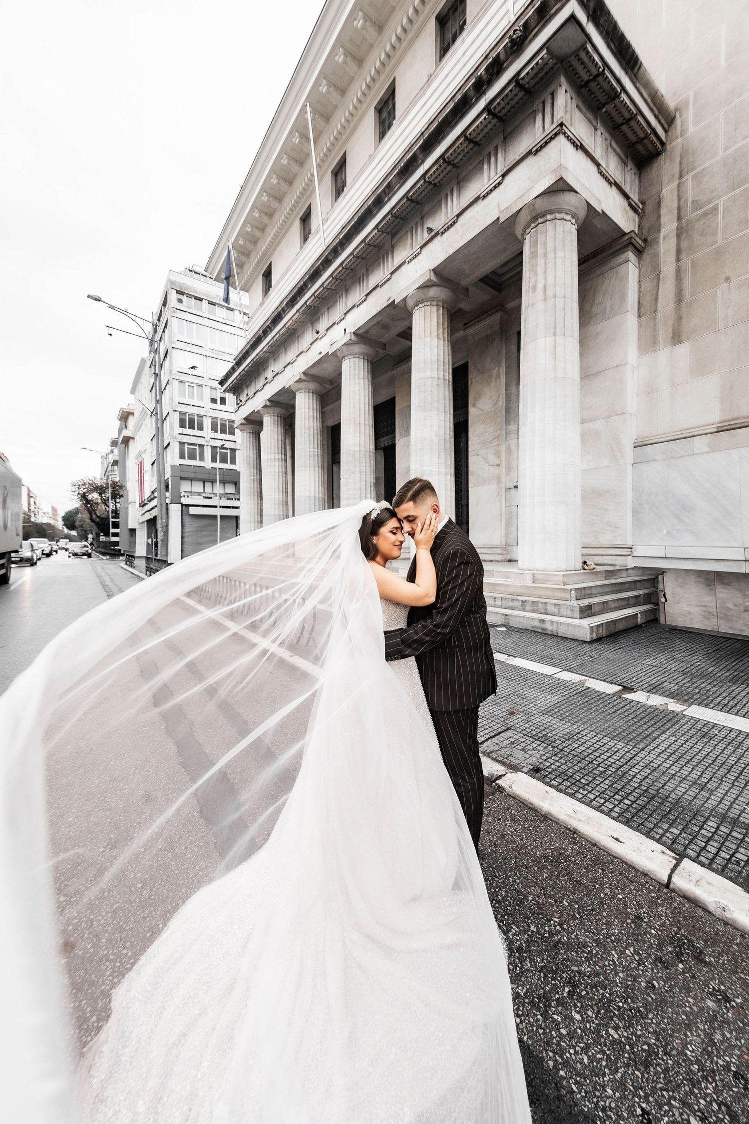 Dramatic wedding photo with flowing veil against neoclassical architecture background.