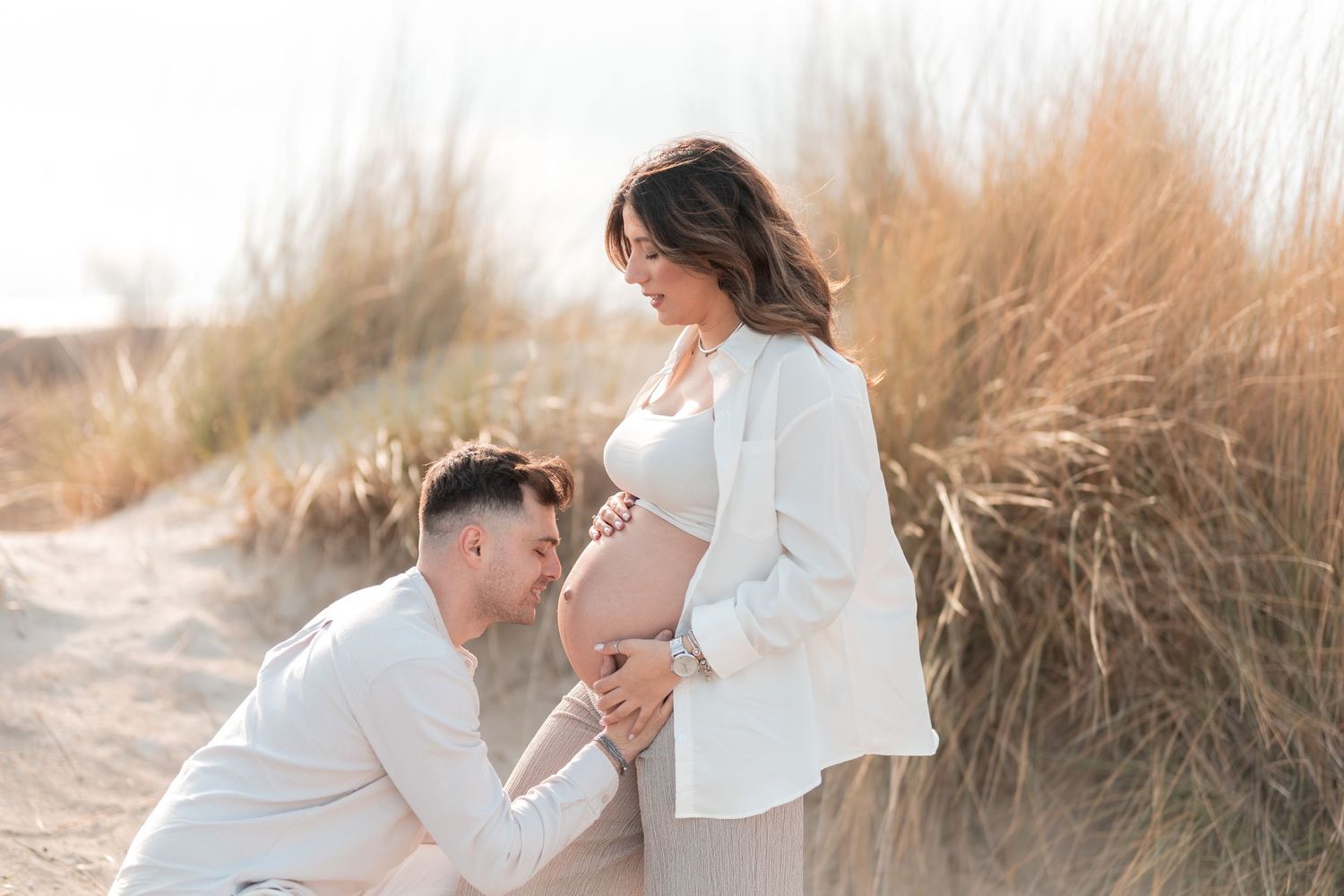 A couple shares an intimate moment together in a sunlit field of tall grass during a romantic photoshoot.