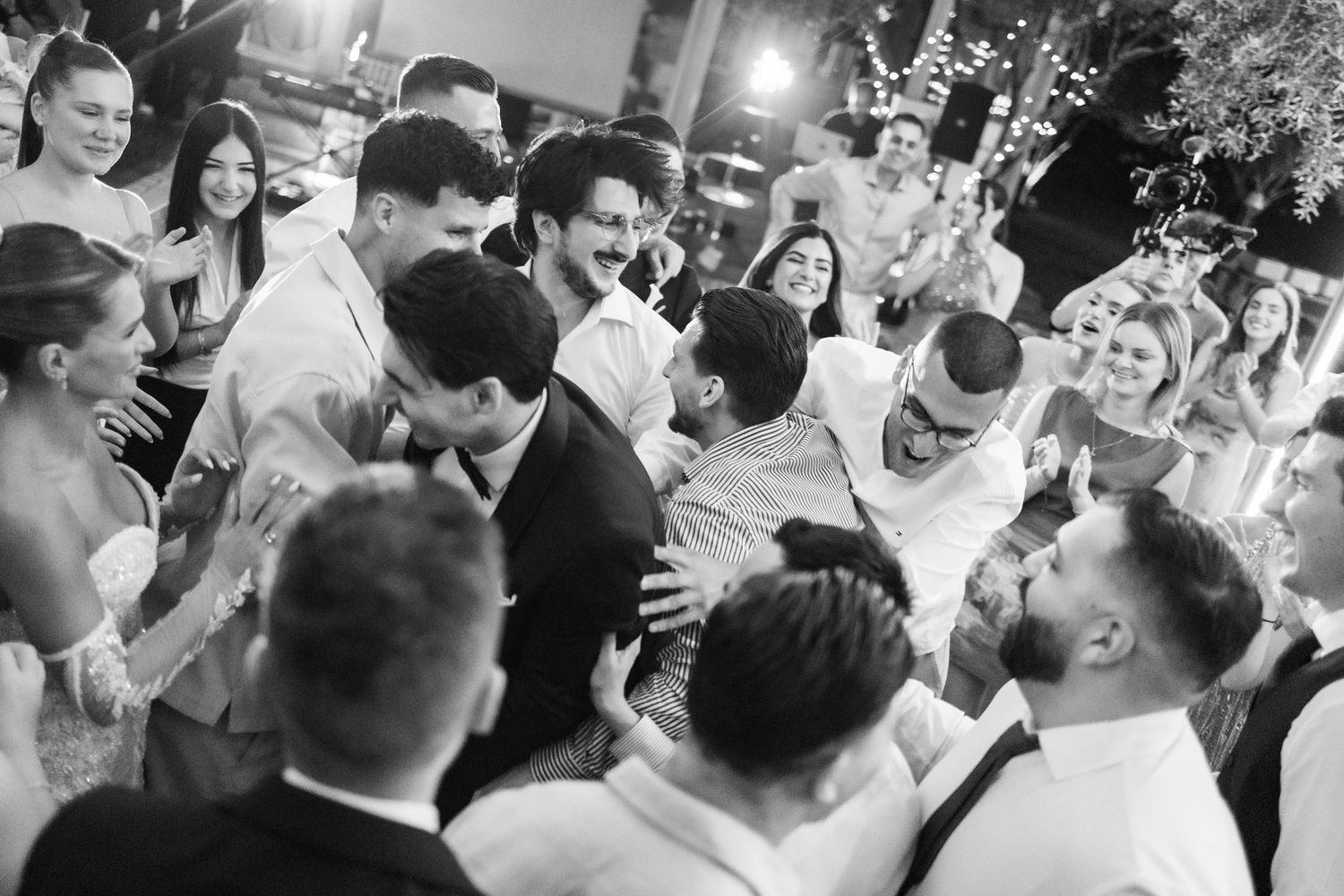 Black and white photo of wedding guests celebrating and dancing together at a lively outdoor reception party.