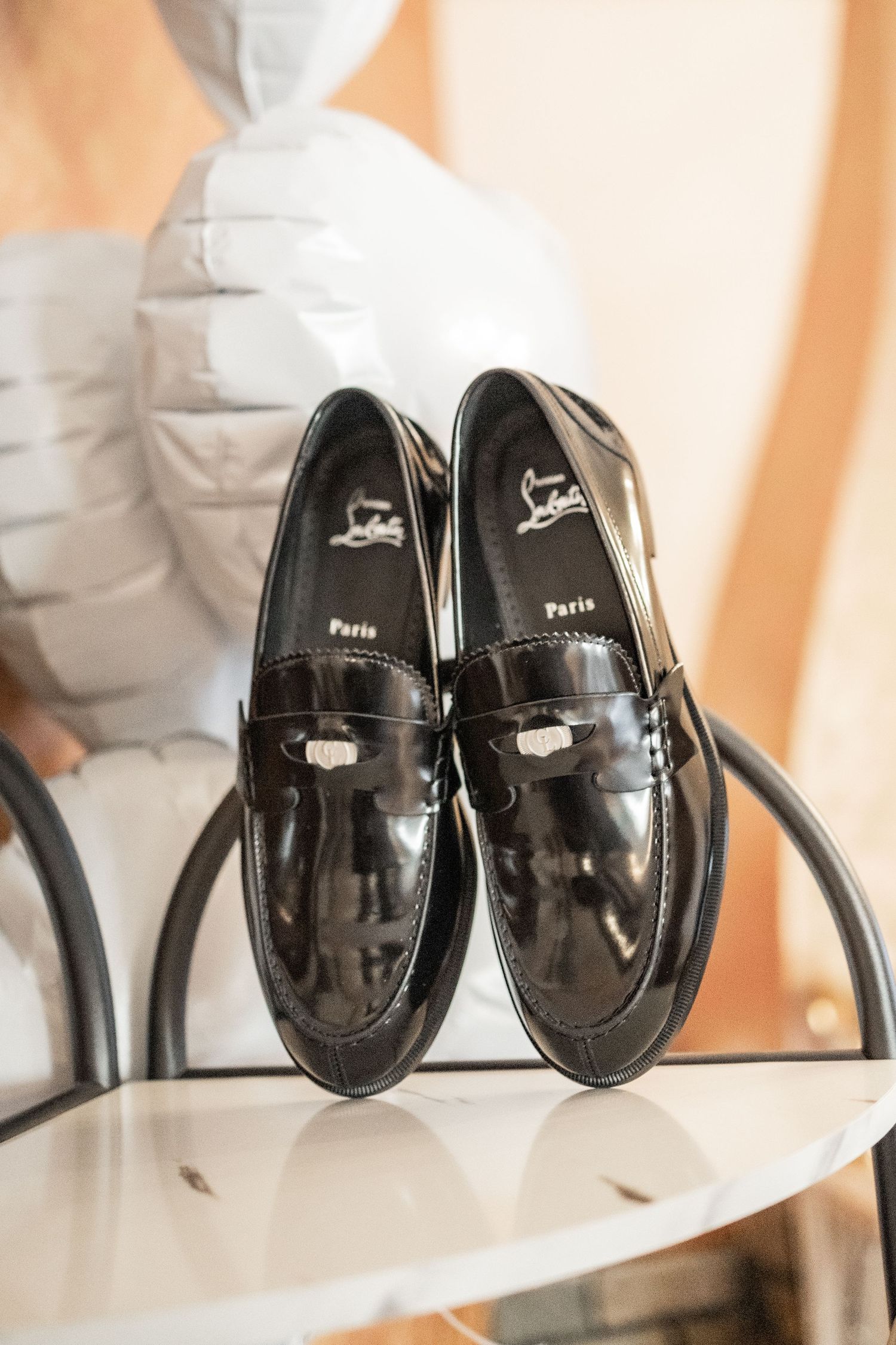 Black patent leather Christian Louboutin penny loafers displayed on a white surface.