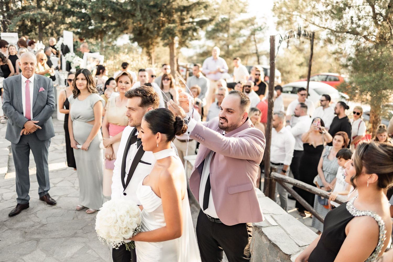 Wedding guests line up outdoors to celebrate the newlyweds during a summer evening celebration.