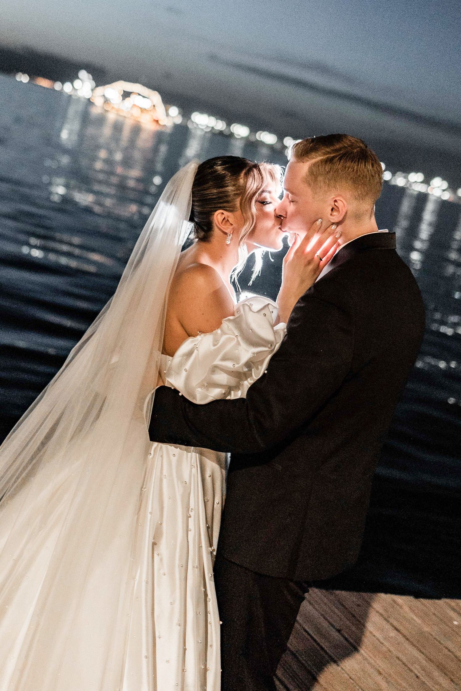 Nighttime wedding portrait with city lights twinkling across water in background.