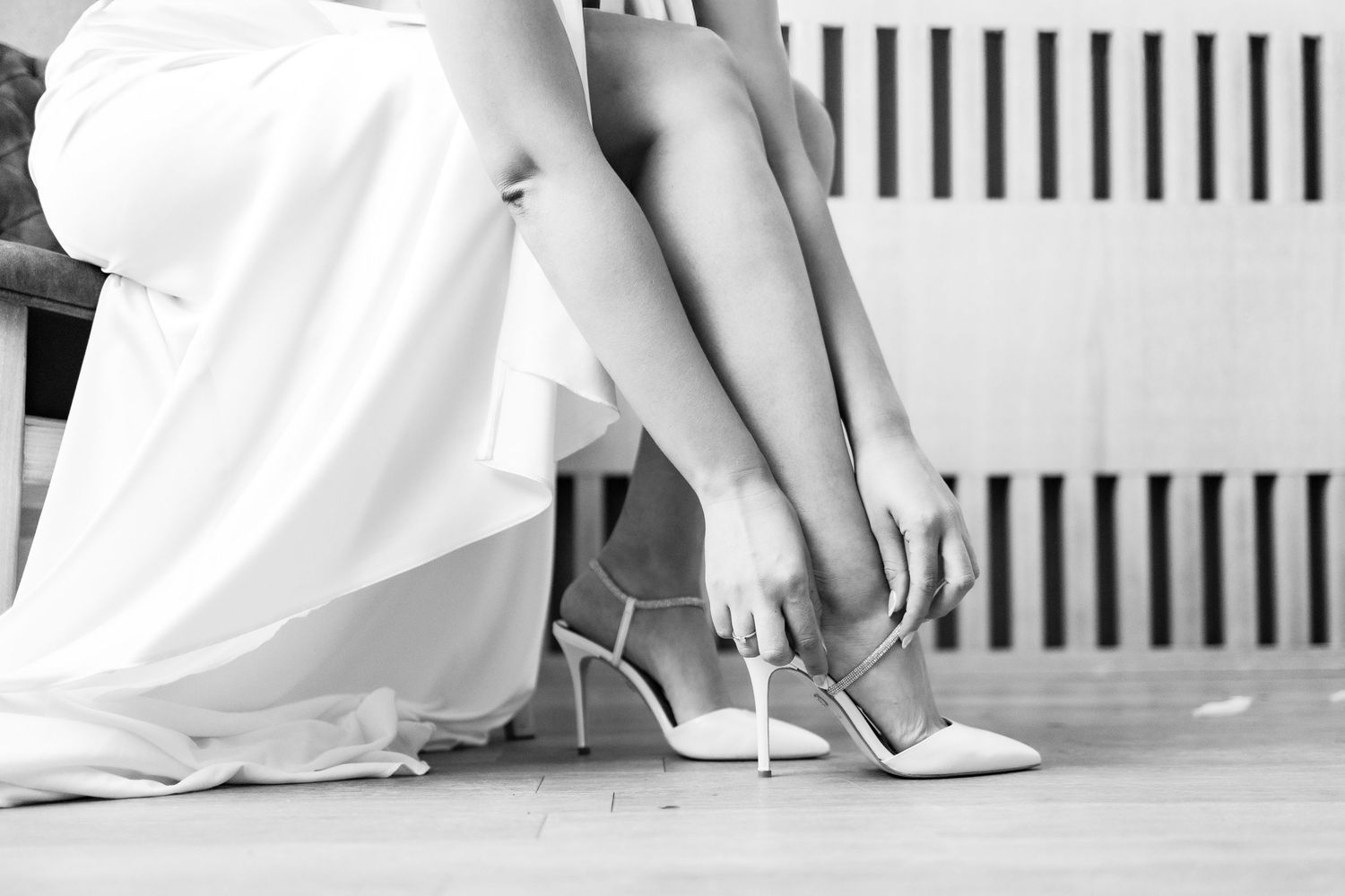 Black and white artistic detail shot of a flowing white wedding dress against dark background.