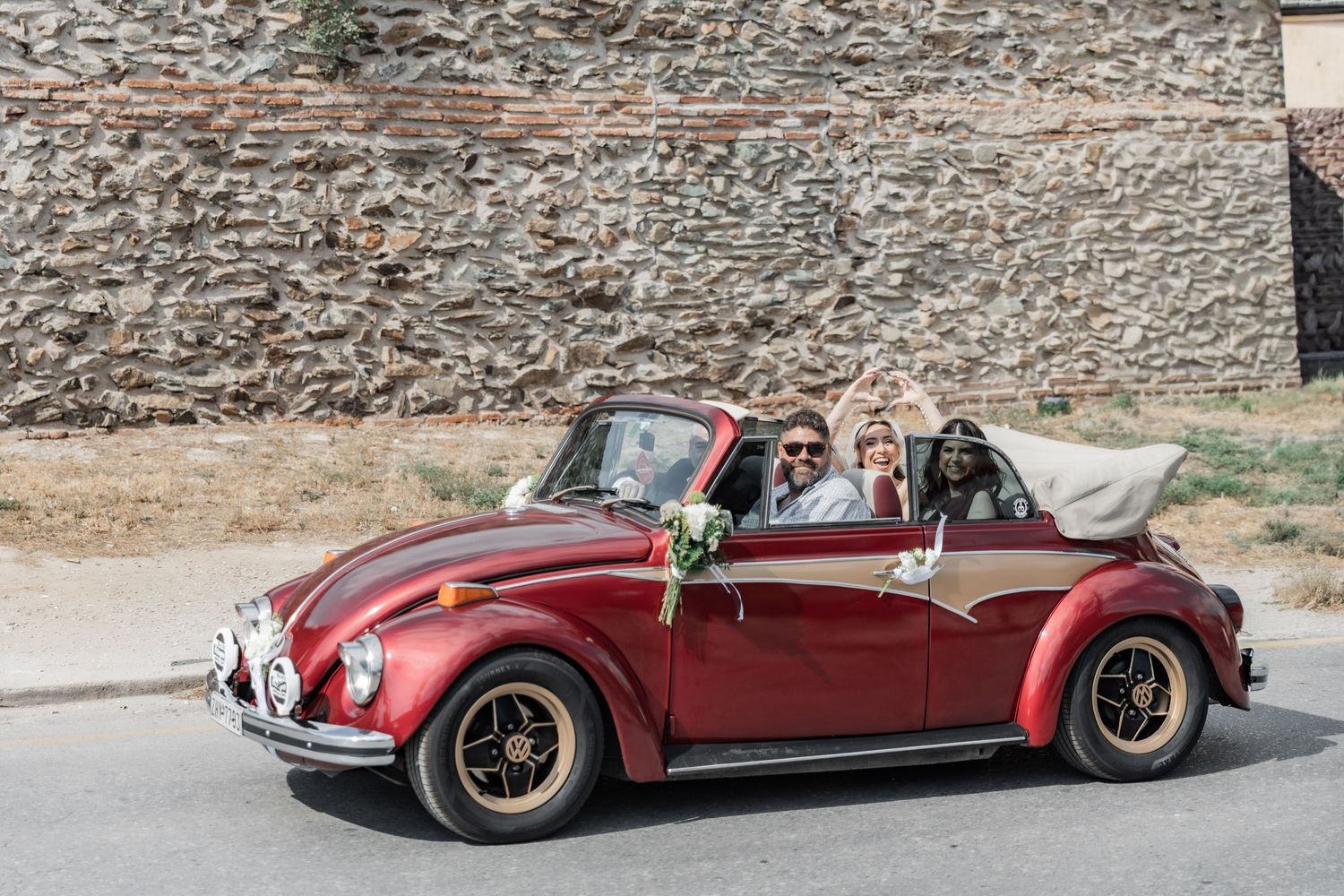 Couple celebrating in a red convertible VW Beetle classic car, decorated with flowers for a wedding.