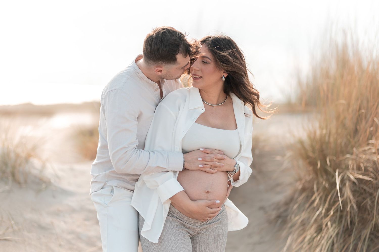 A couple in white outfits embraces tenderly in a golden field at sunset.