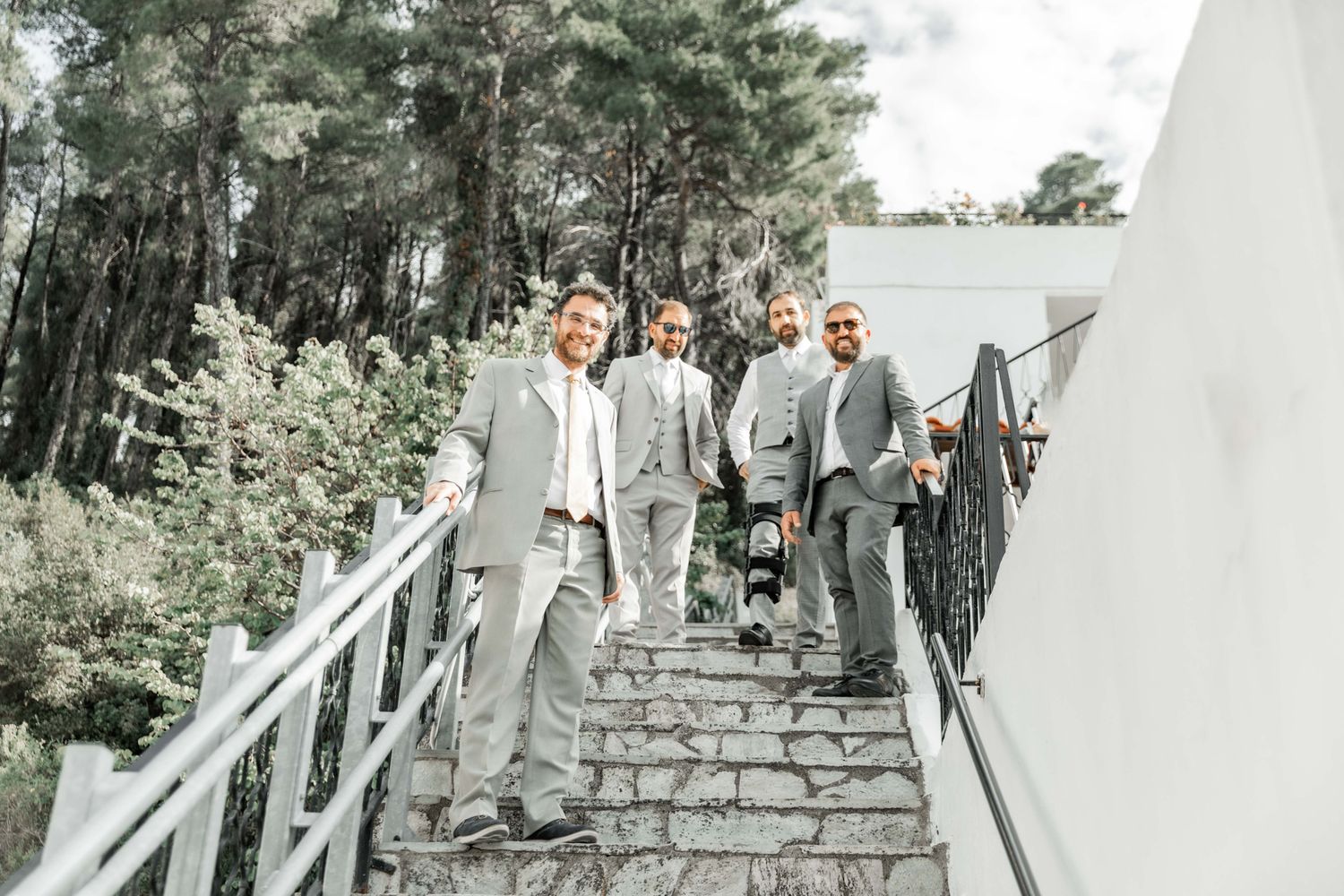 Wedding party members walk up stone steps outdoors in formal grey attire.
