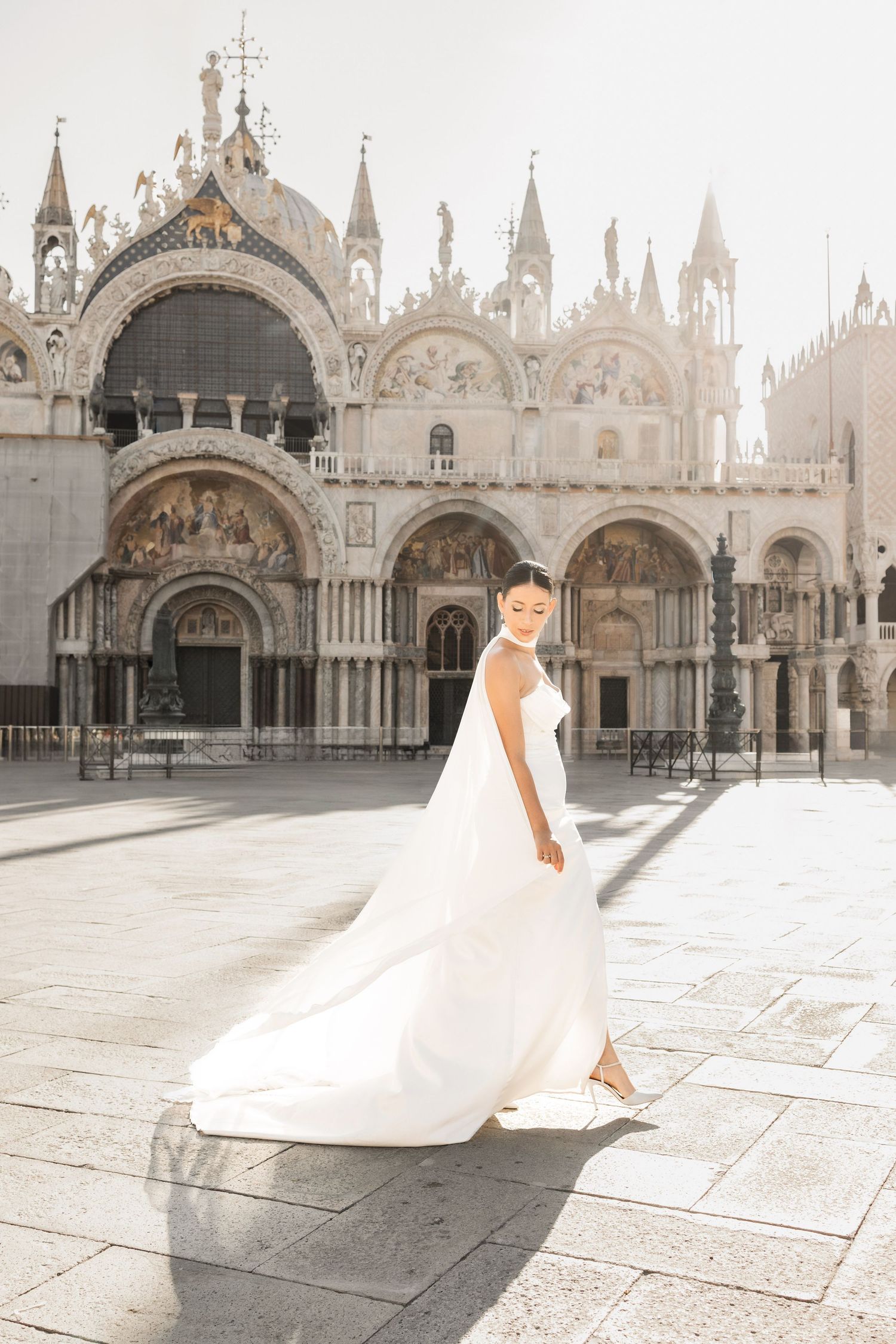 Bride in flowing white dress posing in front of St. Mark's Basilica in Venice.