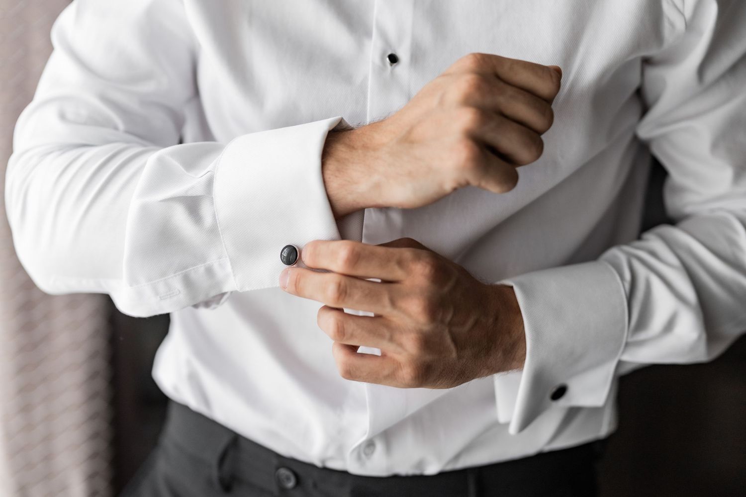 Close-up details of hands adjusting white dress shirt cuffs and buttons.