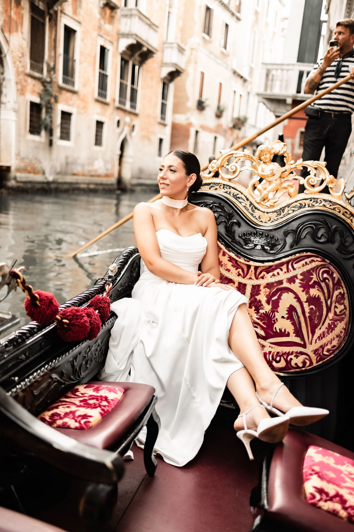 Elegant bride poses in a gondola with luxurious red velvet upholstery in Venice.