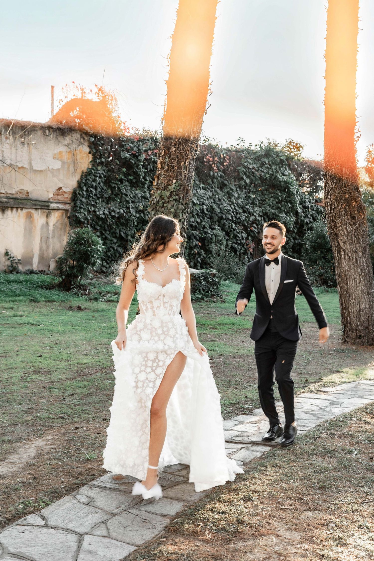 Couple walking along a stone path with ivy-covered walls in an outdoor garden setting.