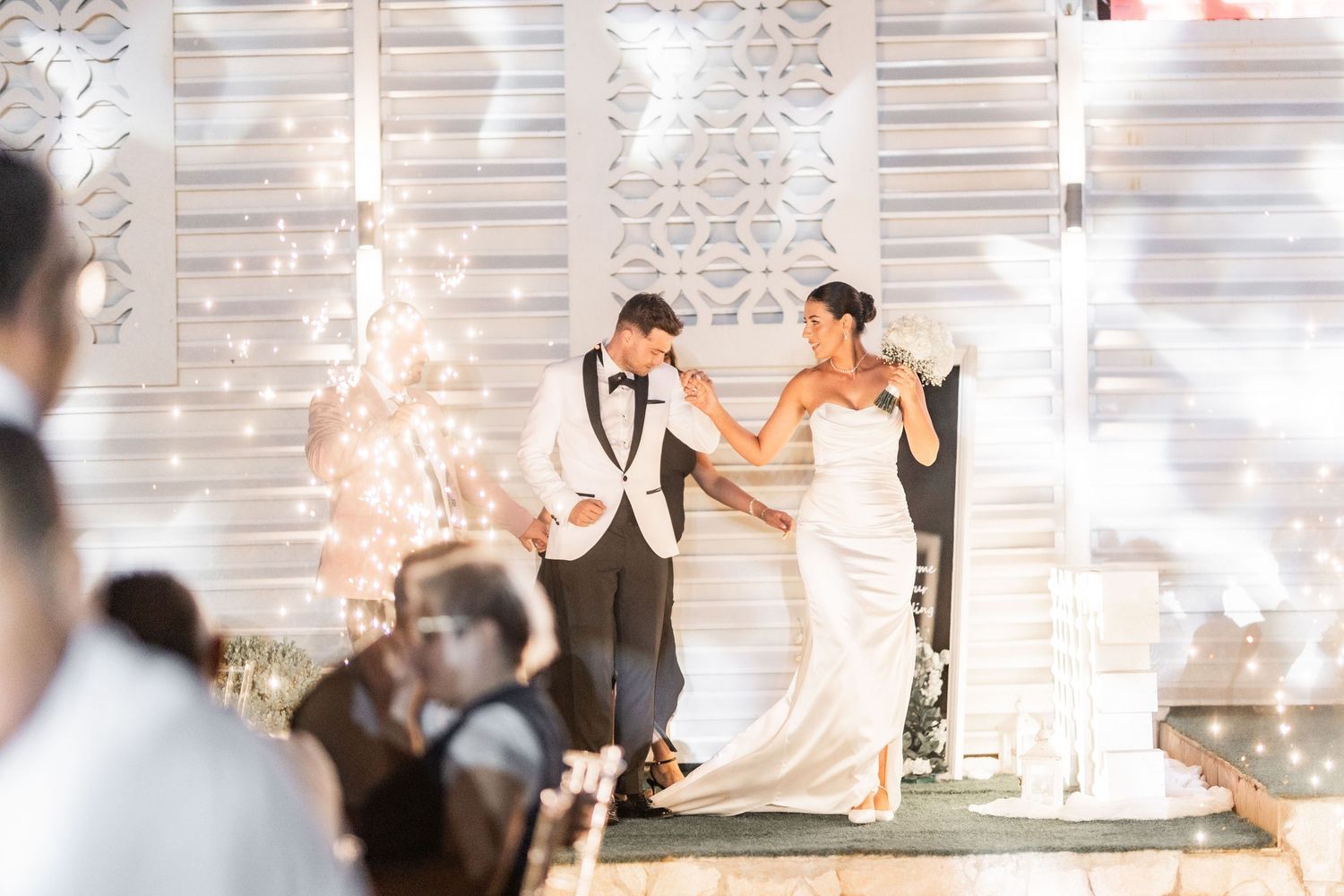 Wedding couple shares romantic dance under twinkling lights at evening reception.