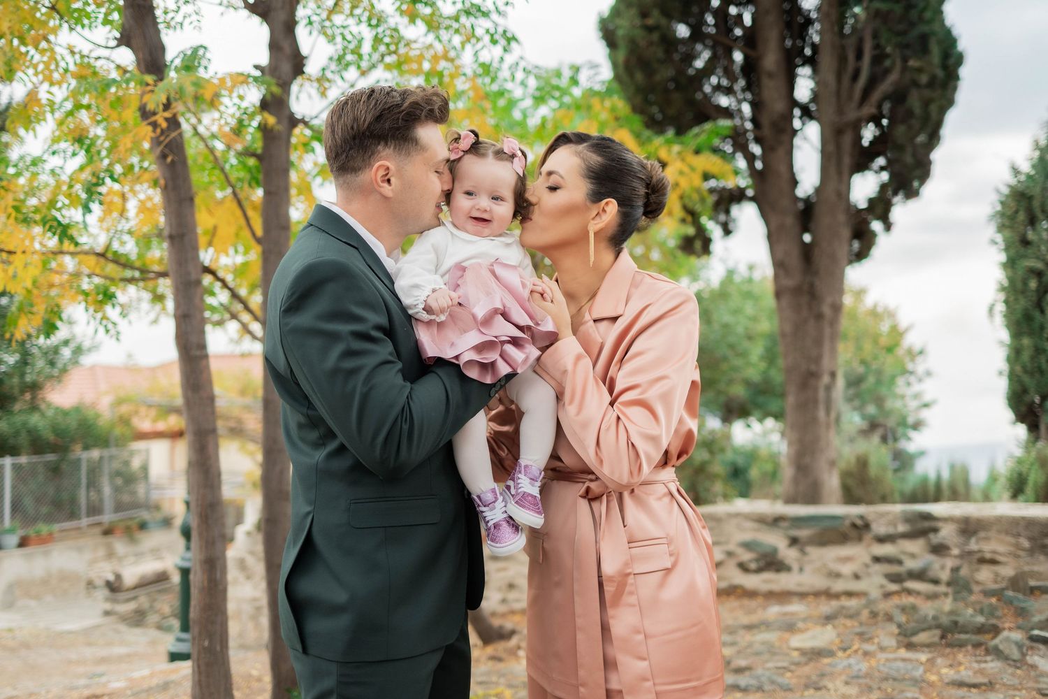 A couple in formal attire shares a romantic moment in a garden setting with autumn foliage in the background.