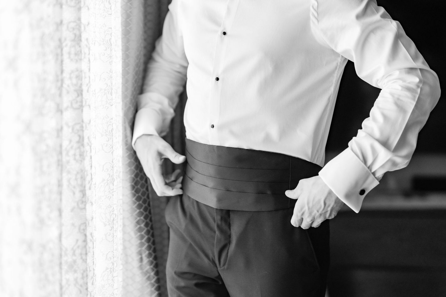 Wedding preparation photos showing details of white shirt and dark pants against window light.