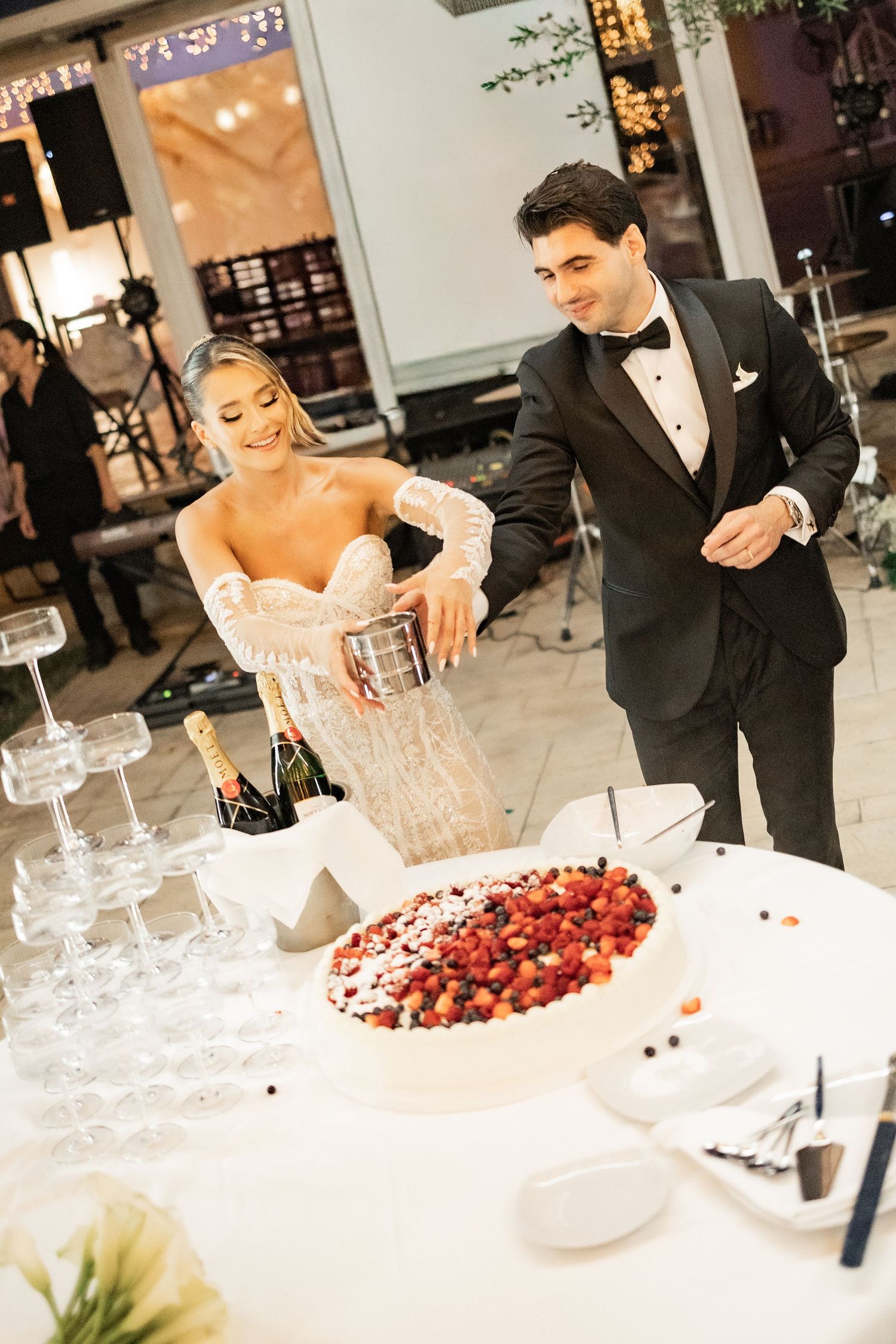 Bride and groom cutting a strawberry wedding cake beside a champagne tower at their elegant reception.
