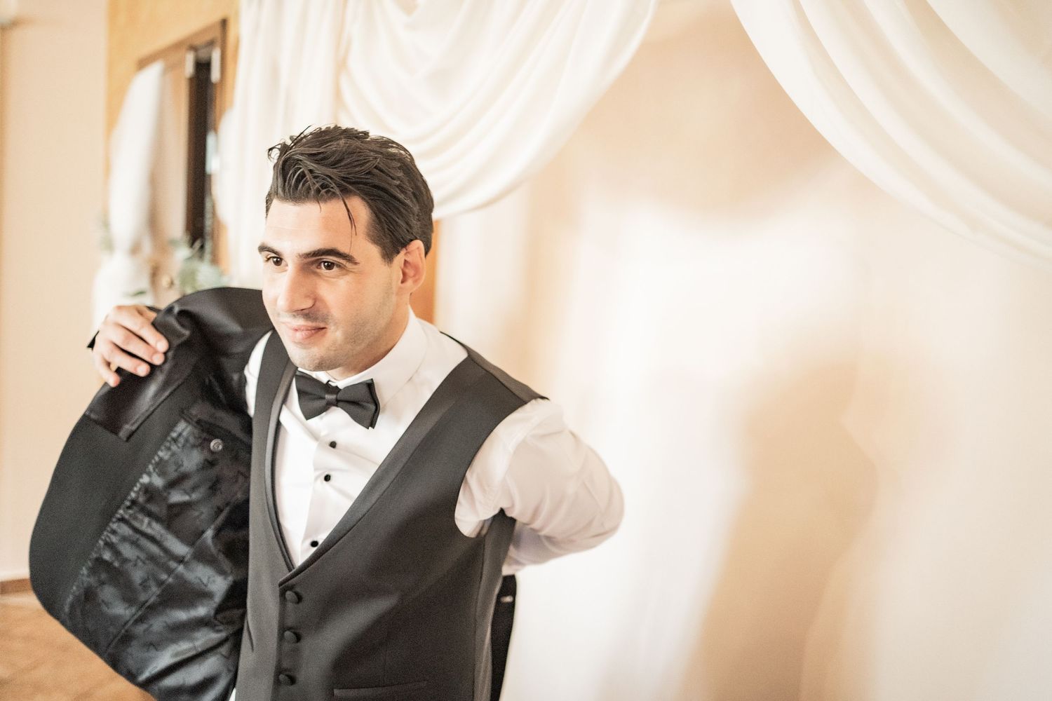 Groom in a black vest and bow tie putting on his suit jacket before the wedding ceremony.