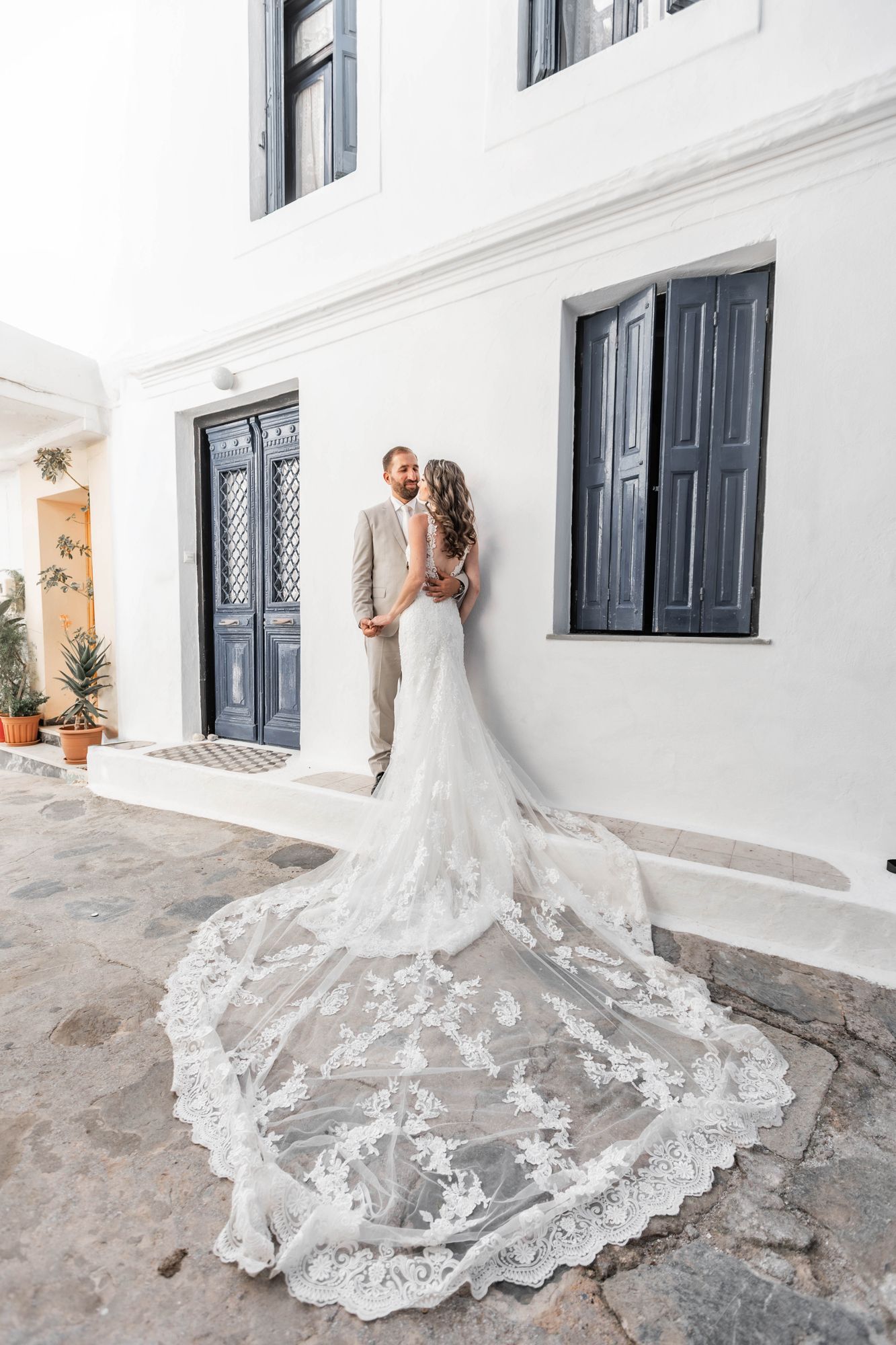 Wedding photo showcasing intricate lace train against white Mediterranean architecture.
