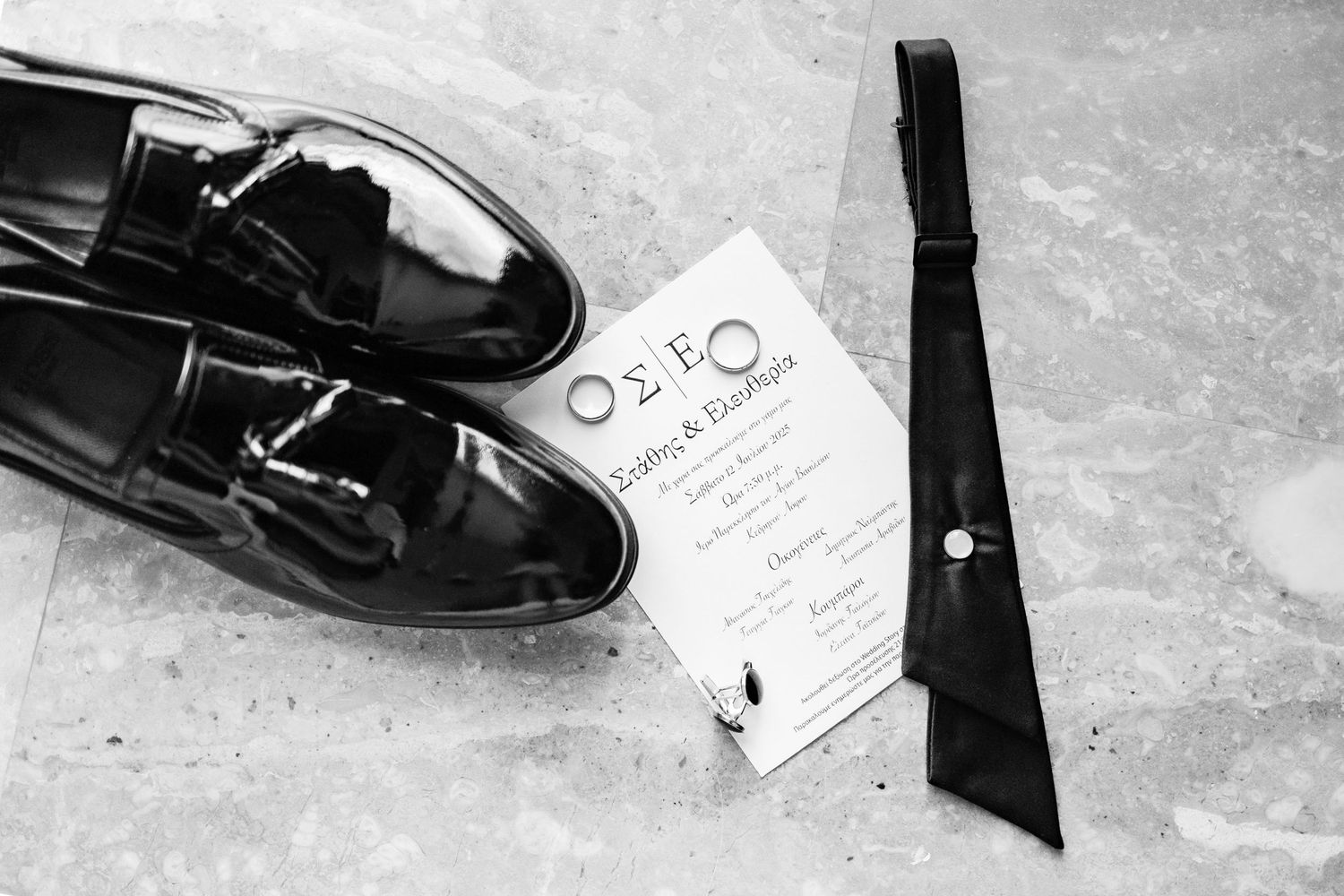 Close-up details of black dress shoes and wedding stationery on textured surface.