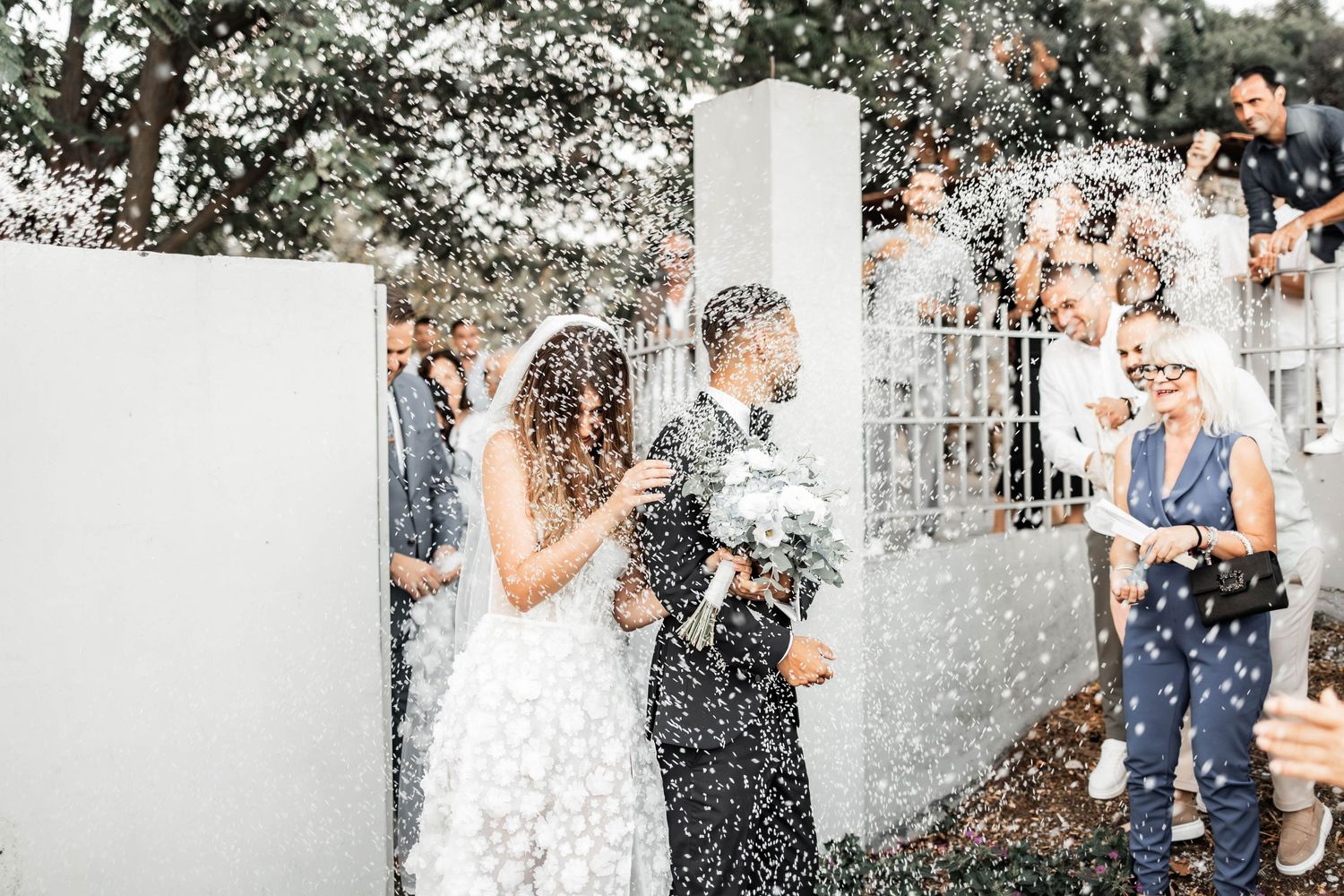 Wedding celebration with guests throwing confetti outdoors on a sunny day.