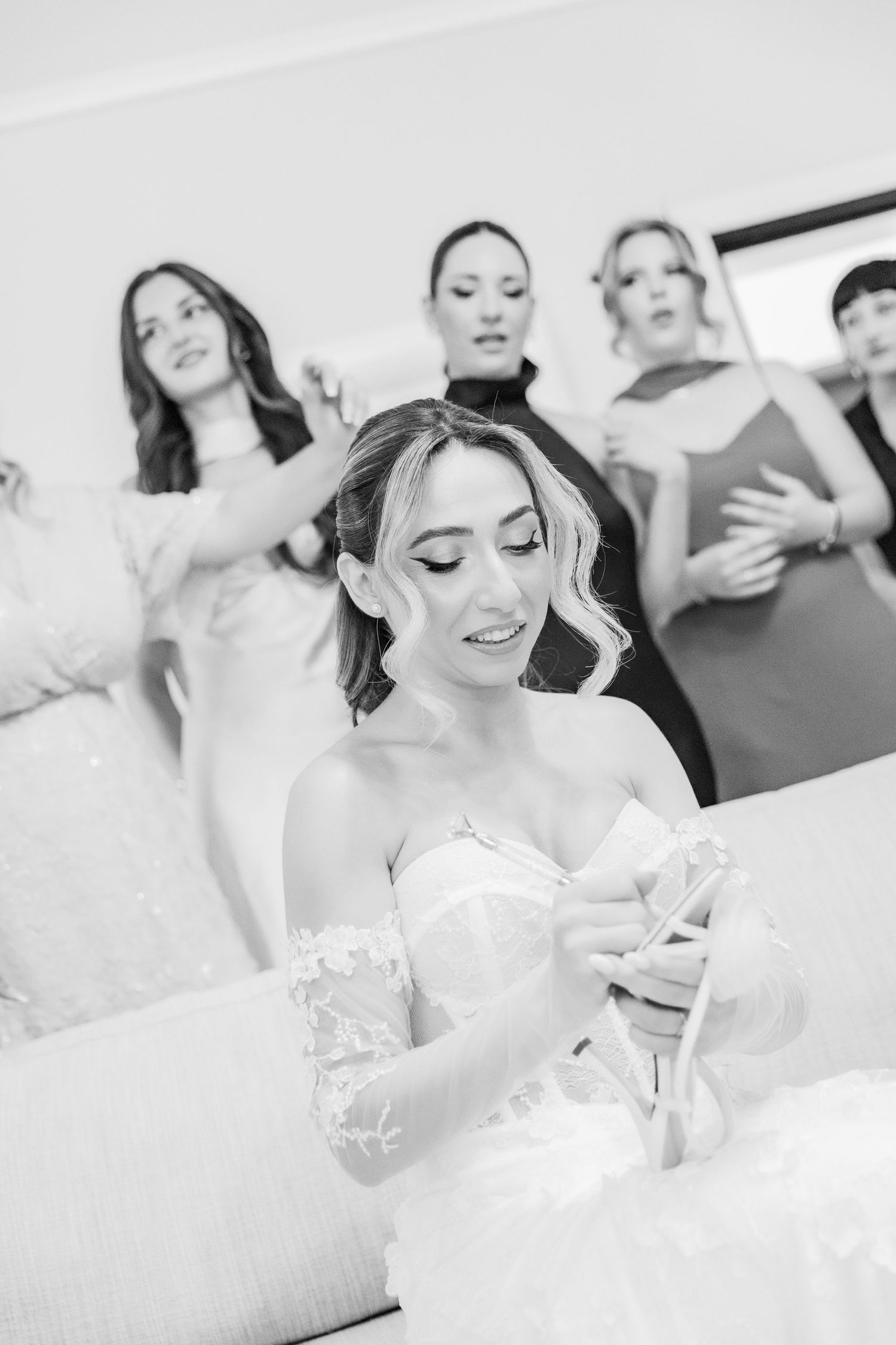 Black and white photo of a bride holding her wedding shoe while bridesmaids react with excitement behind her.