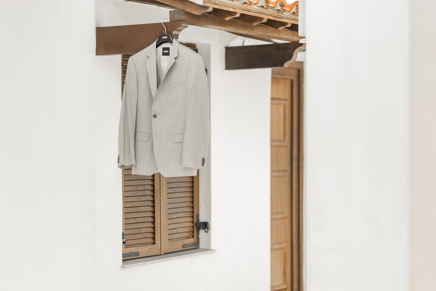 A light gray suit jacket hanging on display against a white wall with wooden details.