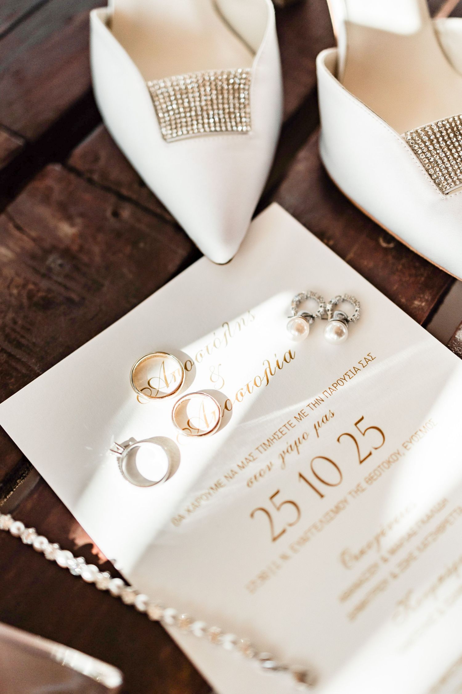 Wedding invitation with gold calligraphy and rings displayed on rustic wooden surface.