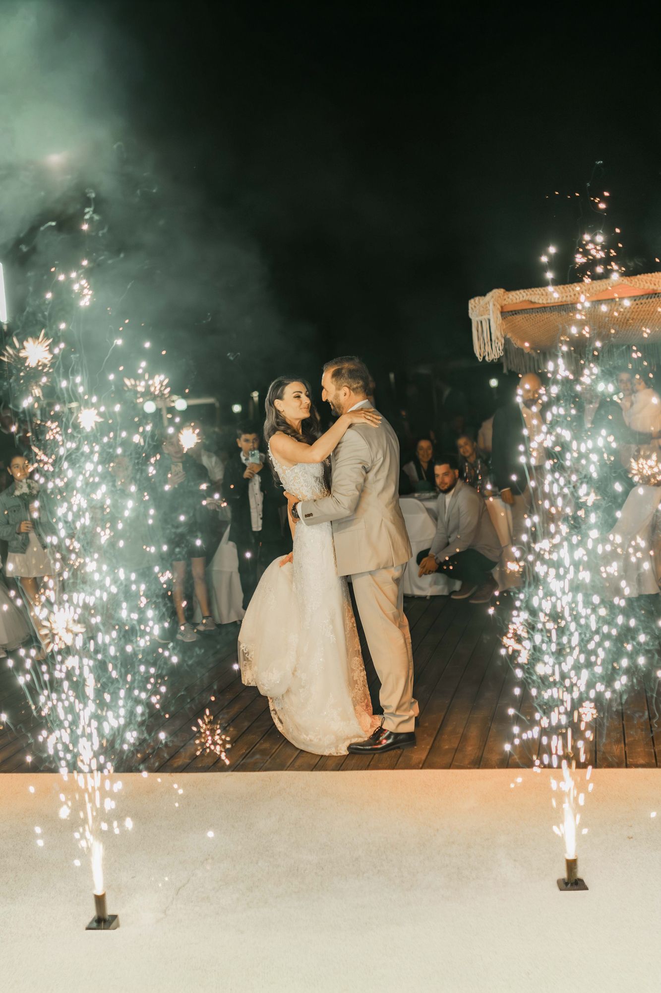 Newlyweds share their first dance surrounded by sparkling fountains at night.