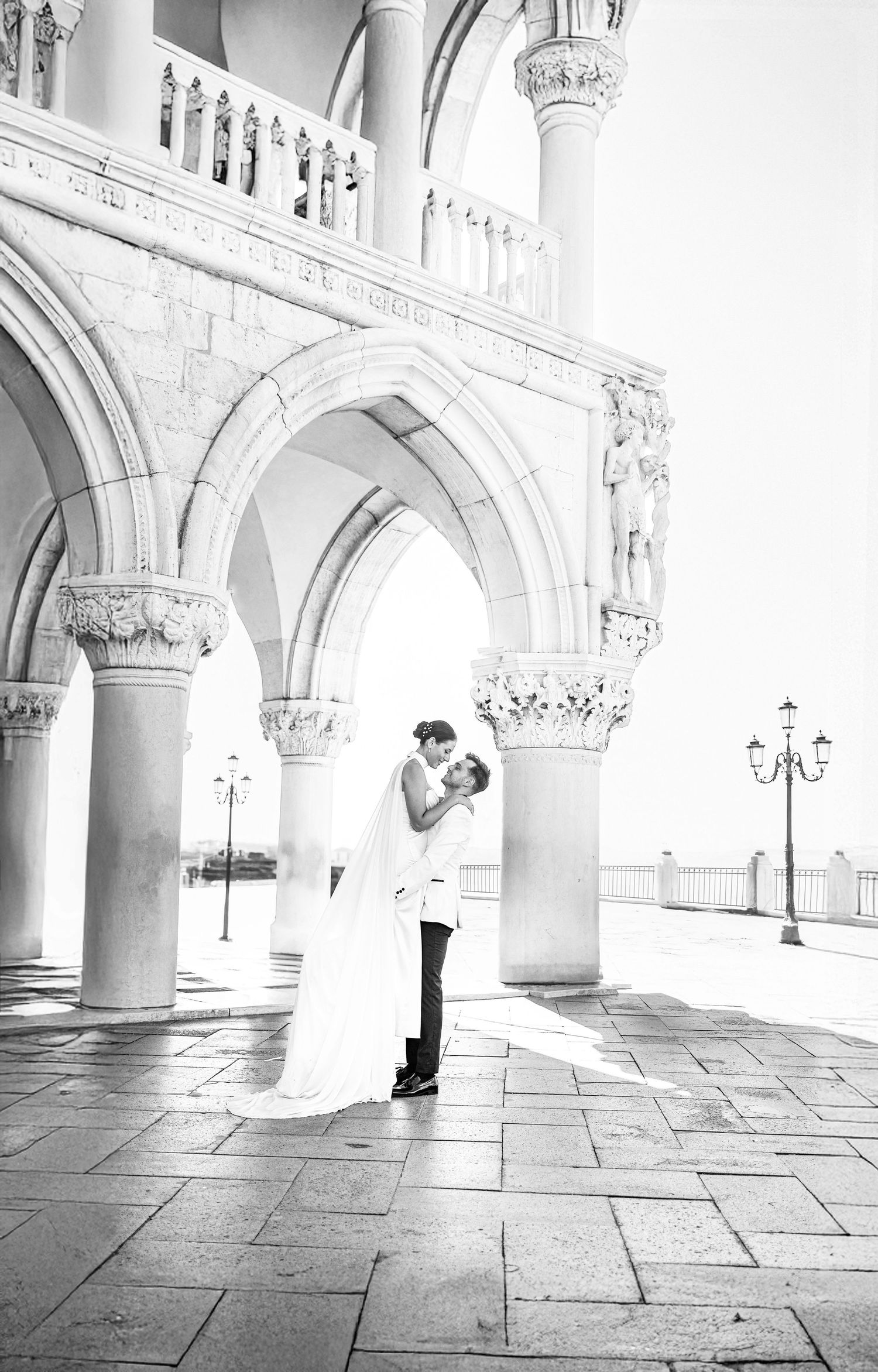 An elegant couple sharing a moment under ornate Venetian Gothic arches in black and white.