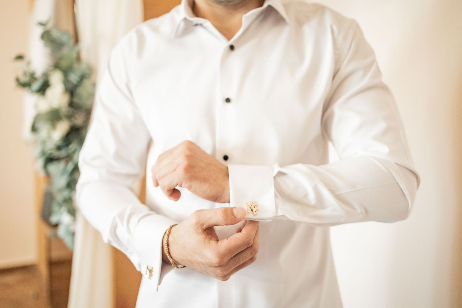 Groom in white dress shirt fastening gold cufflinks while getting ready for wedding ceremony.
