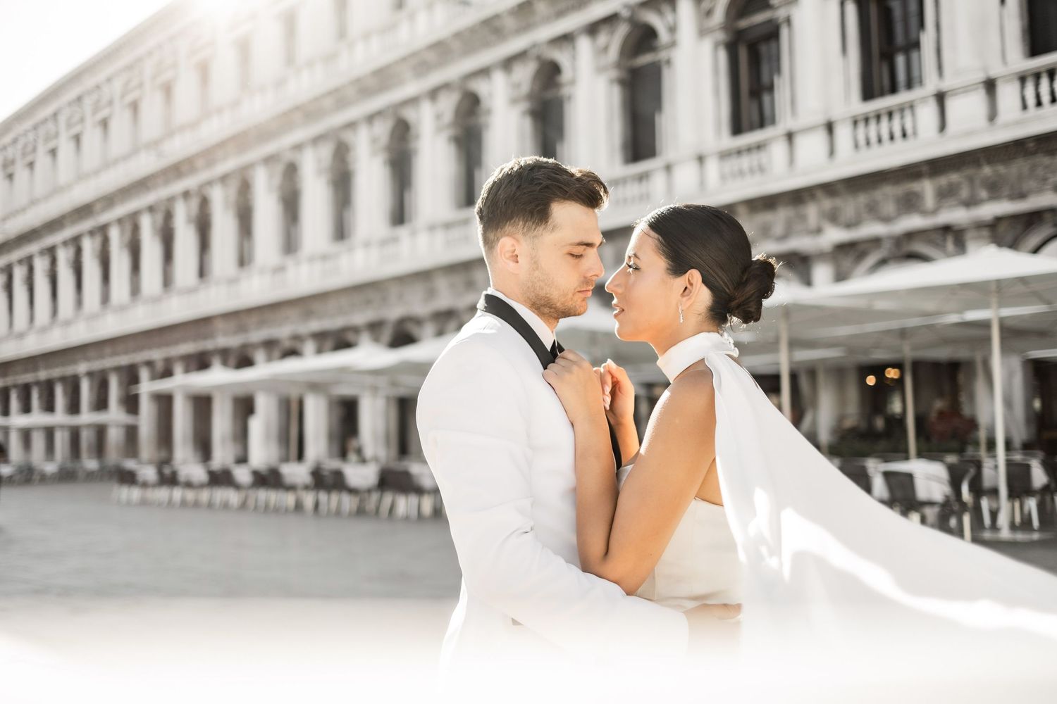A couple sharing an intimate moment in formal attire against historic Venetian architecture.