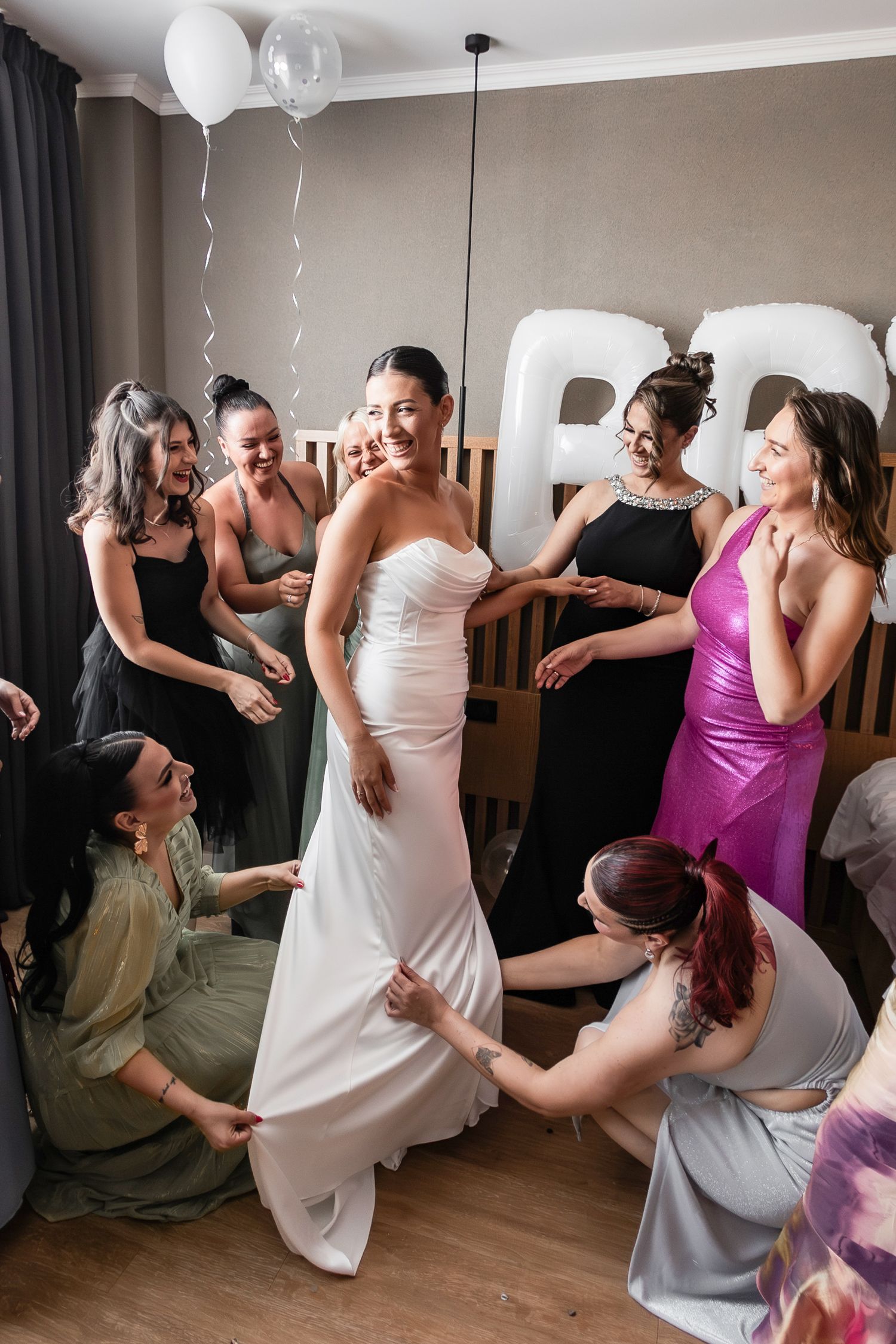 Wedding party helps with final dress adjustments during pre-ceremony preparations.