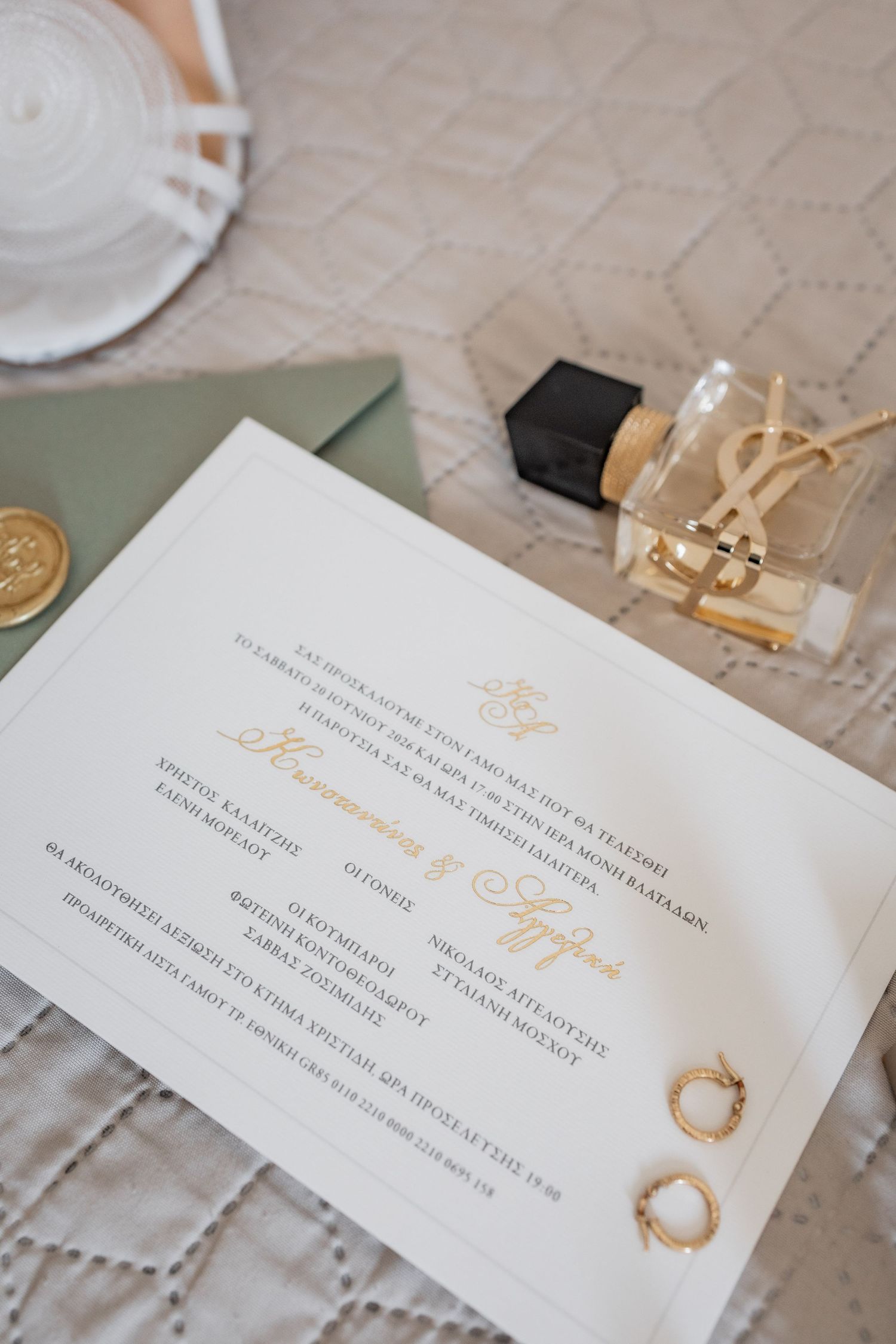 Elegant wedding invitation with gold script, YSL perfume, gold rings, green envelope, and wax seal on white lace.