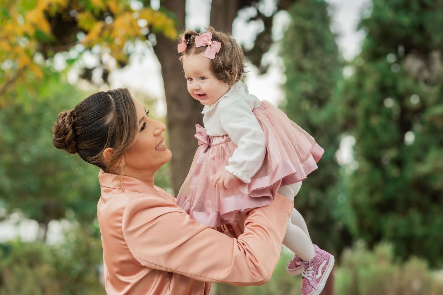 A loving family moment captured outdoors with soft natural lighting and lush greenery in the background.
