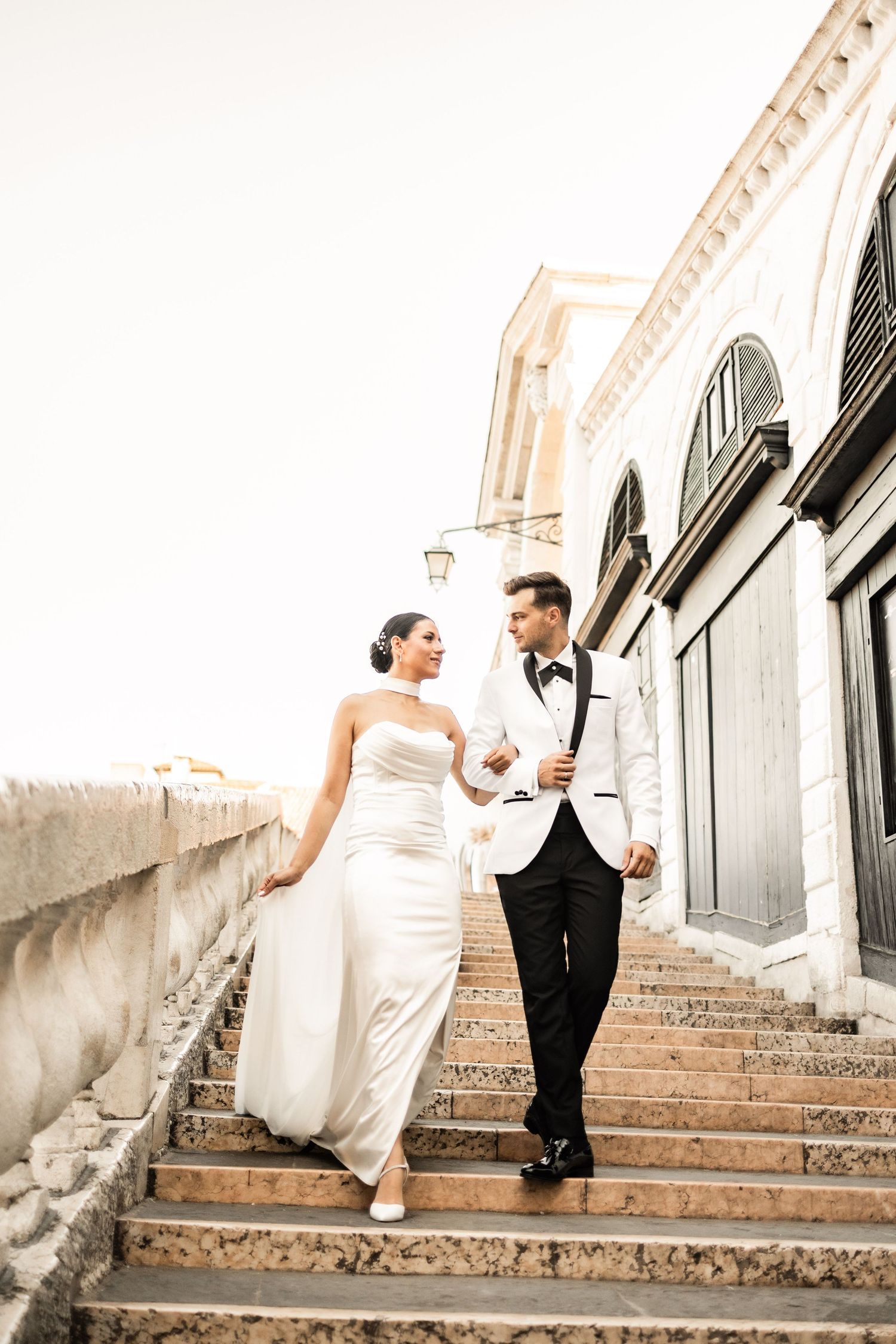 A couple in wedding attire descending stone steps together in Venice.