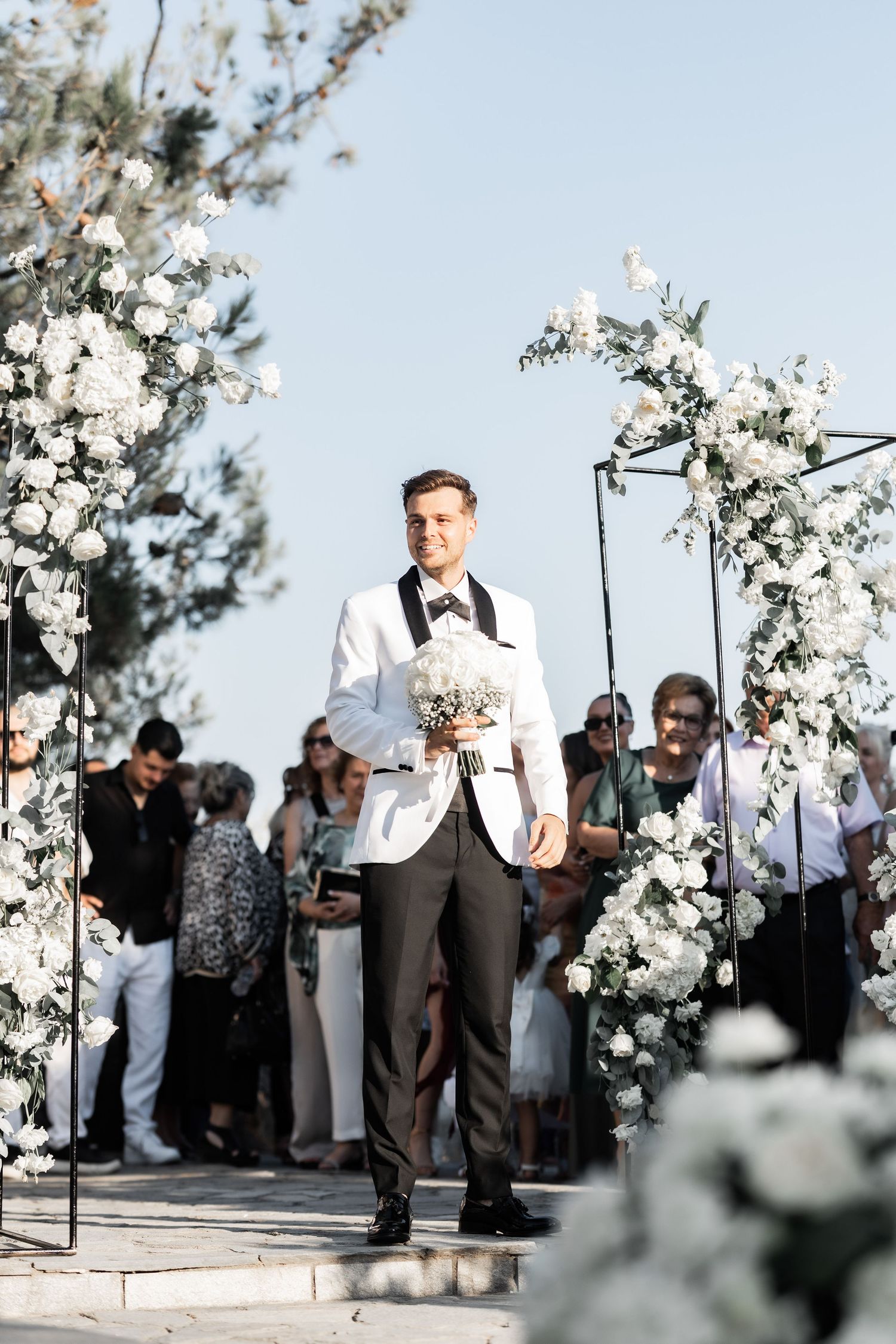 An elegant outdoor wedding ceremony setup with white floral arches and guests gathered.