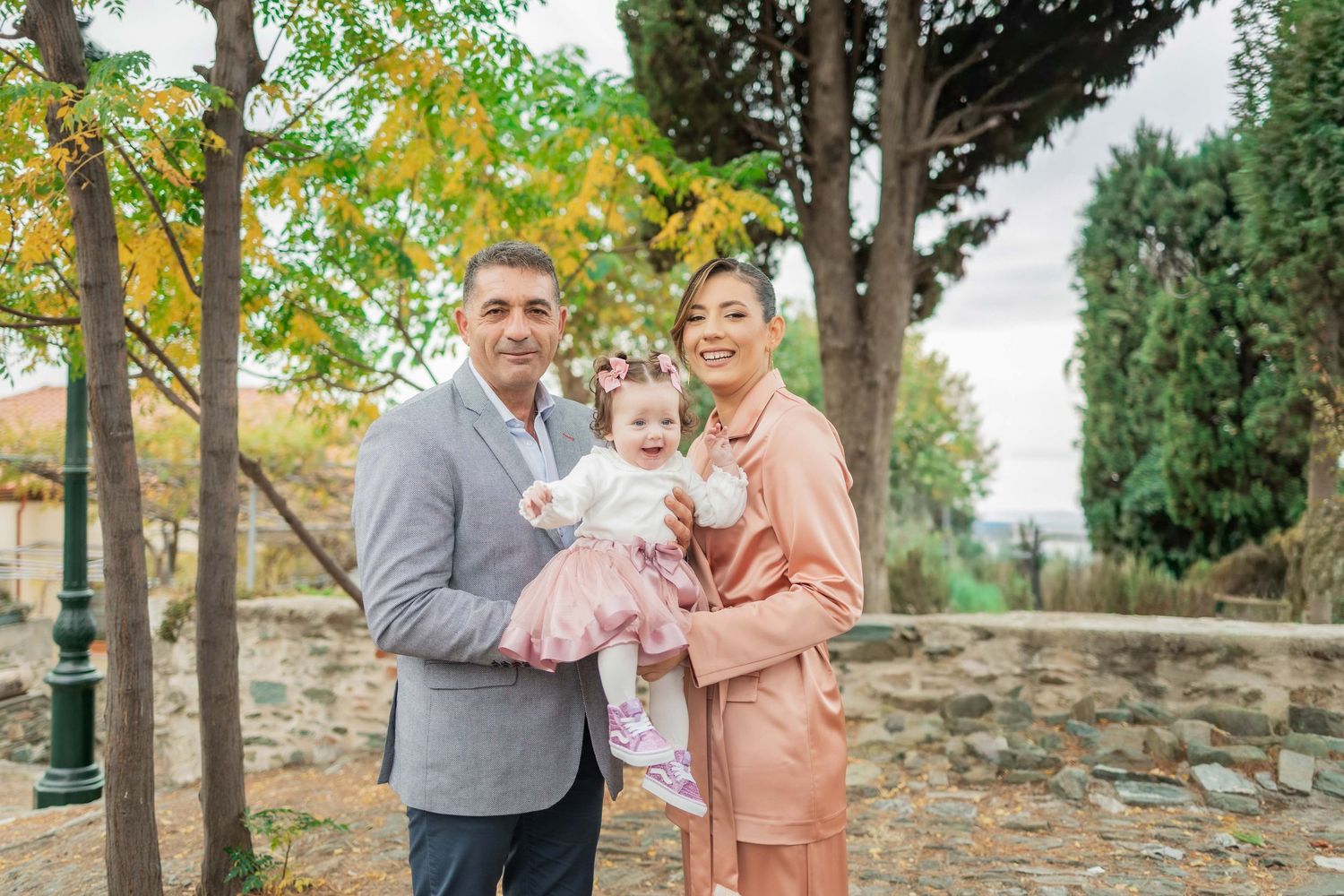 Family group poses together outdoors in a garden setting with trees and greenery in the background.