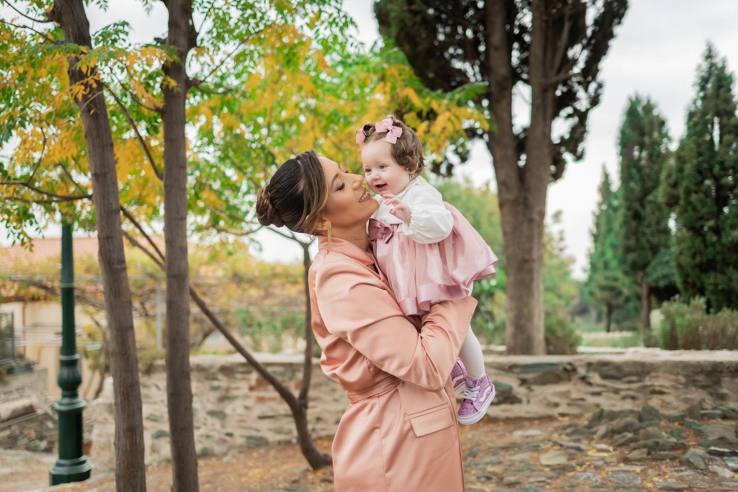 A couple in matching pink outfits shares romantic moments in a scenic outdoor setting during autumn.