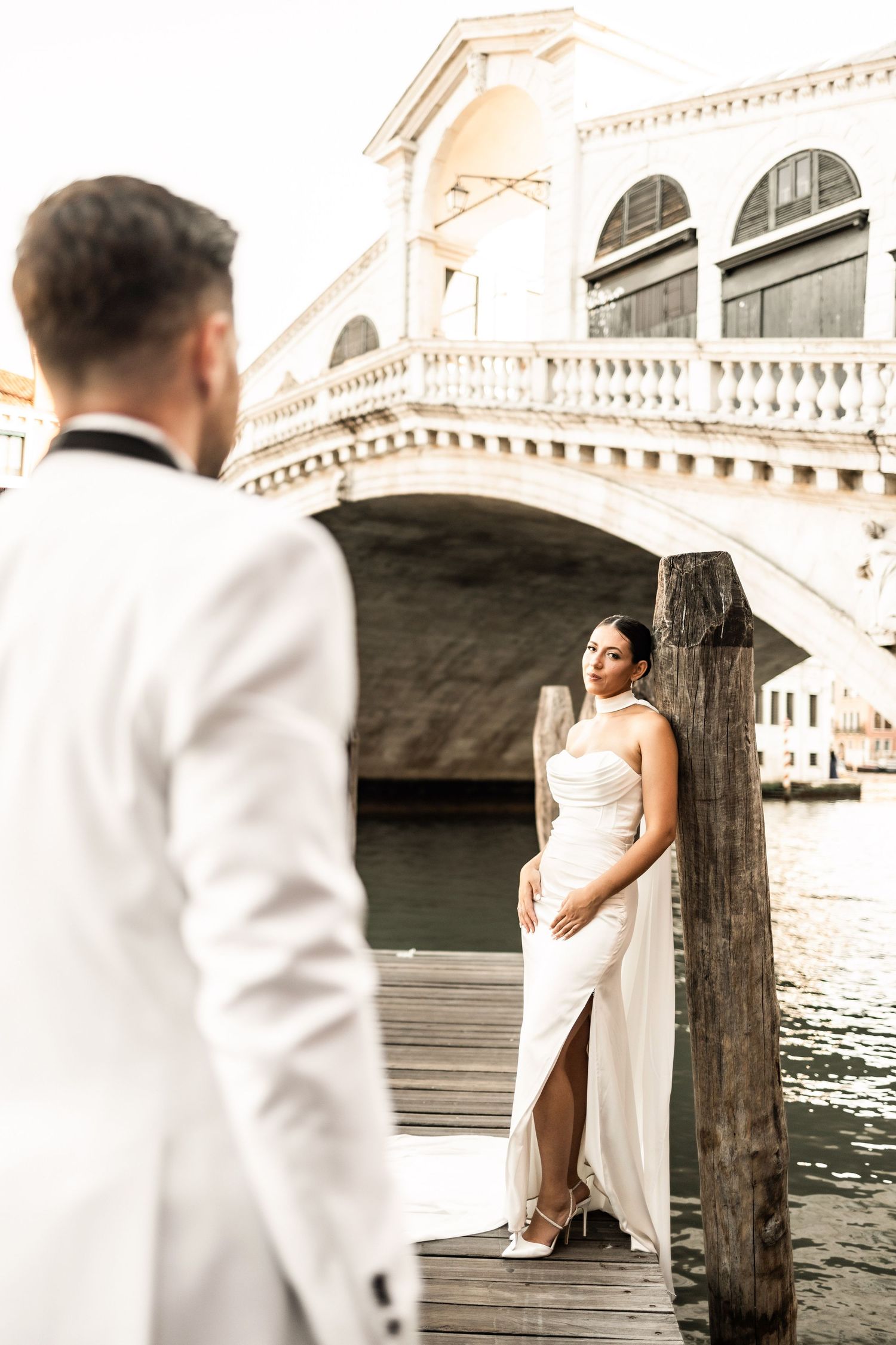 Elegant couple's photoshoot by the canals of Venice with historic bridge backdrop.