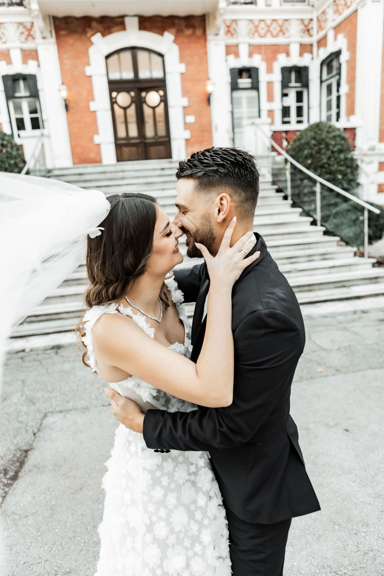 A tender wedding moment captured on the steps of a beautiful brick building with ornate architecture.