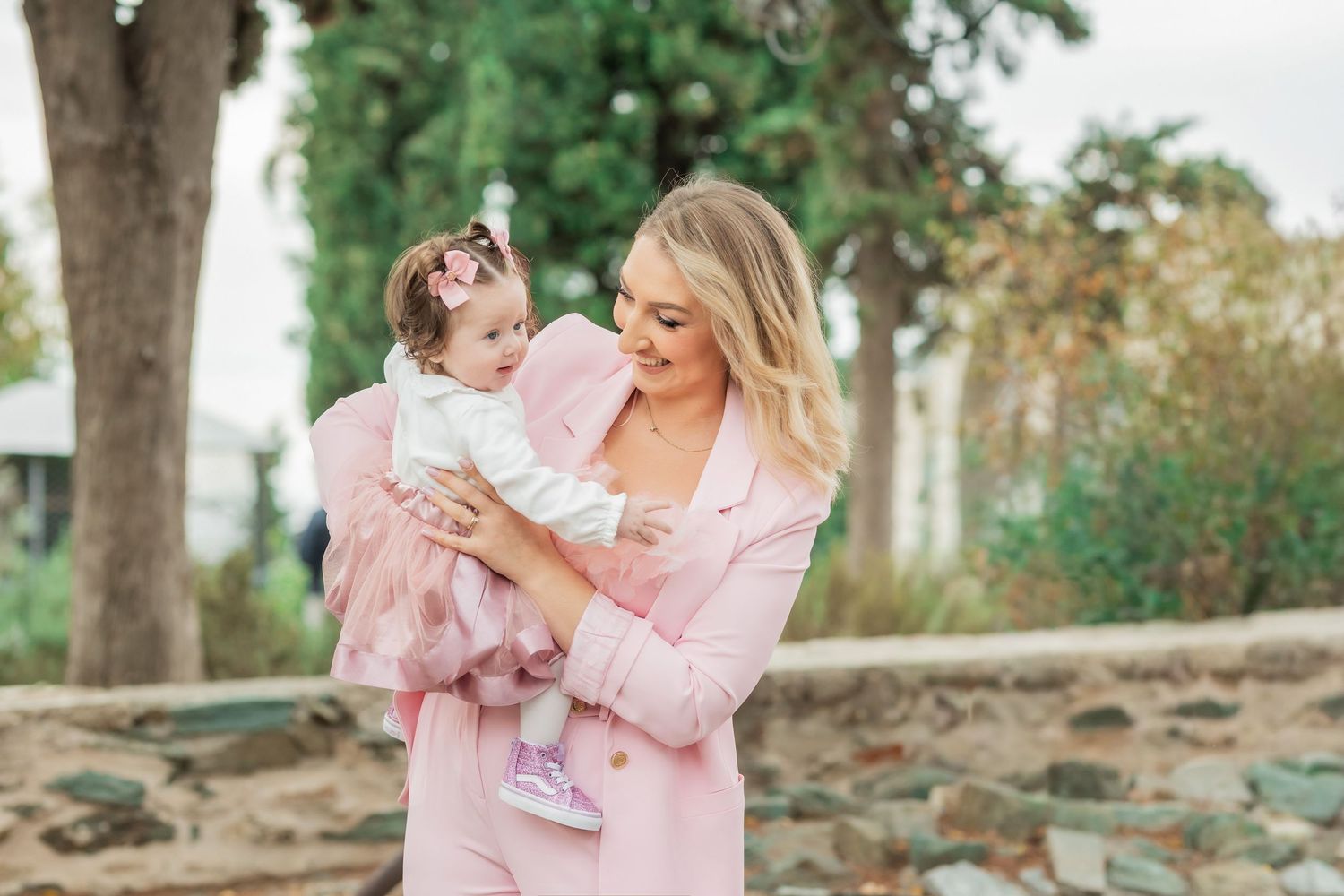 A series of outdoor family photos in a park setting with pink and neutral tones showing tender moments together.