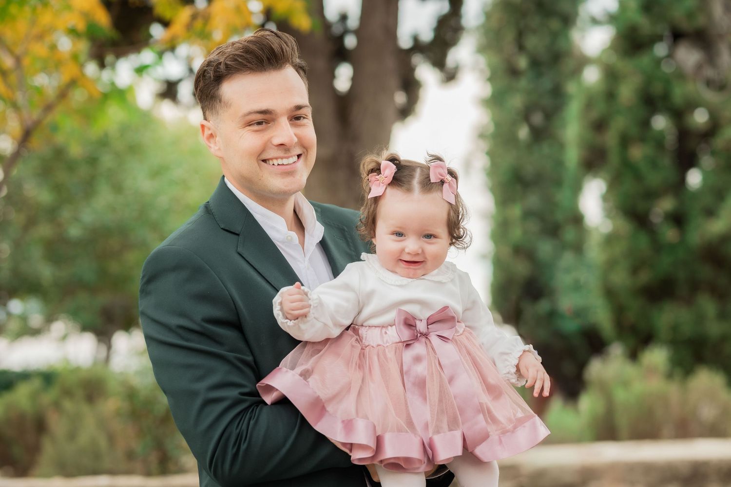 A baby in a pink dress is being held outdoors during a fall photo session.