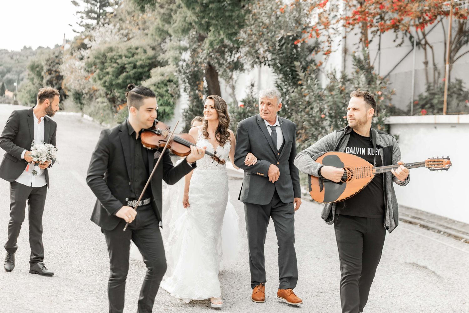 Wedding musicians perform with string instruments during an outdoor ceremony.