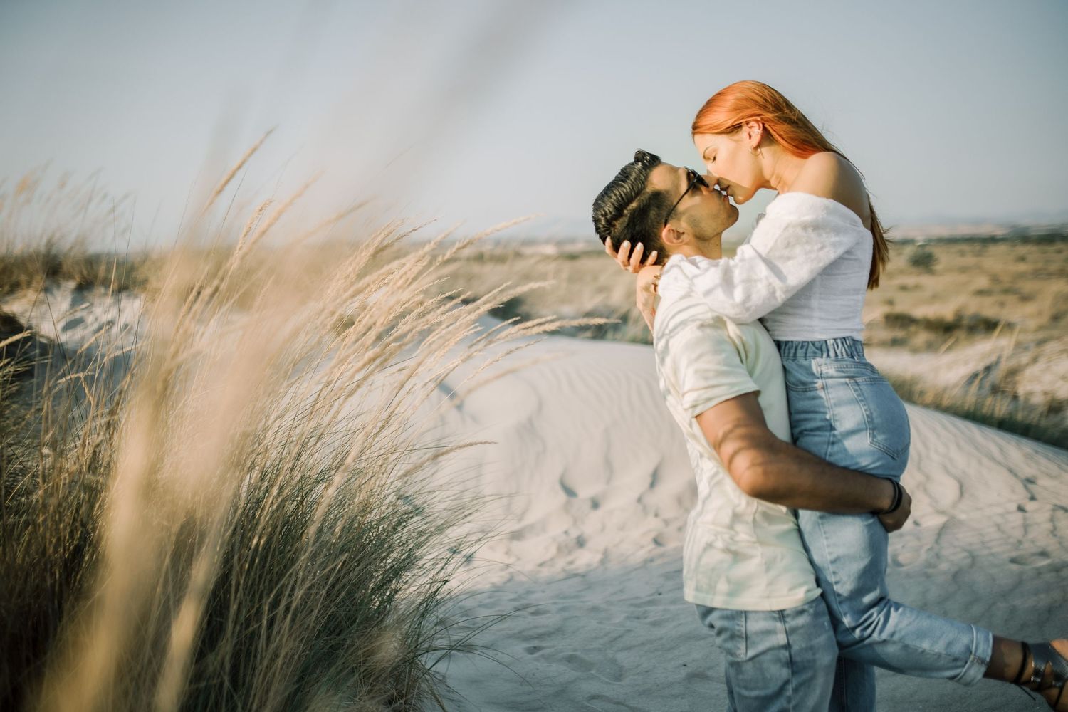 A couple embraces in a romantic moment on a sandy beach during golden hour.