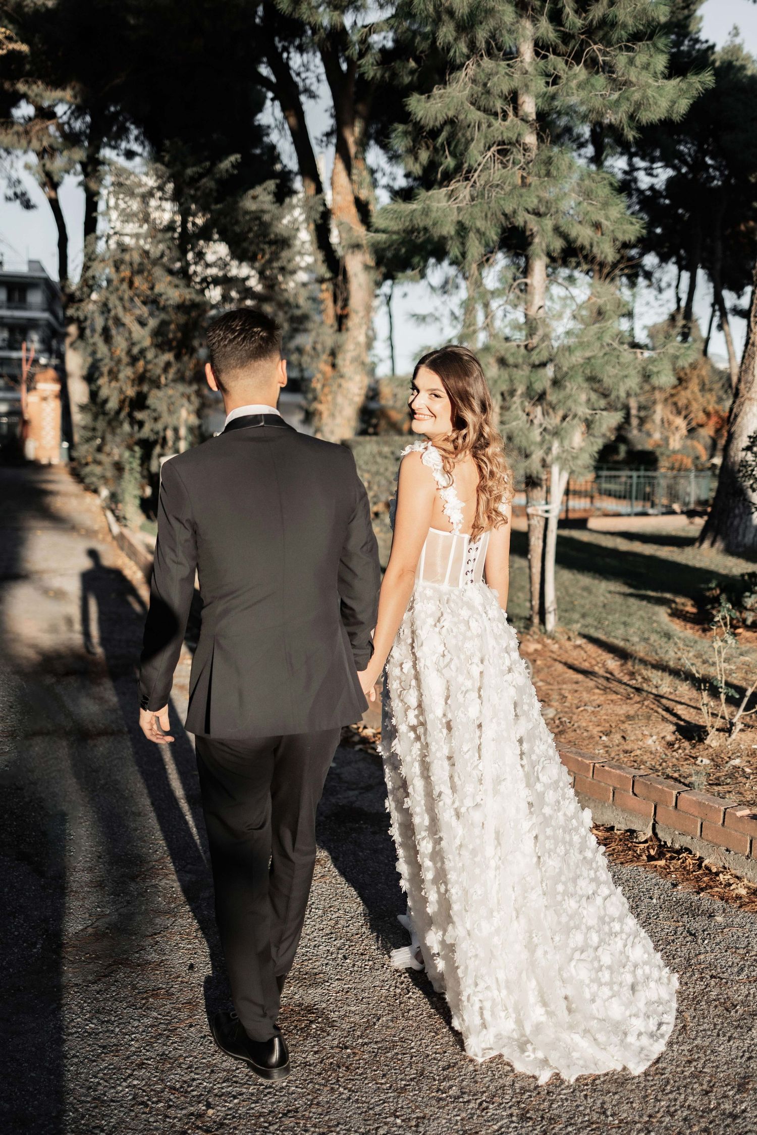 Newlyweds walking together on a tree-lined path during sunset.