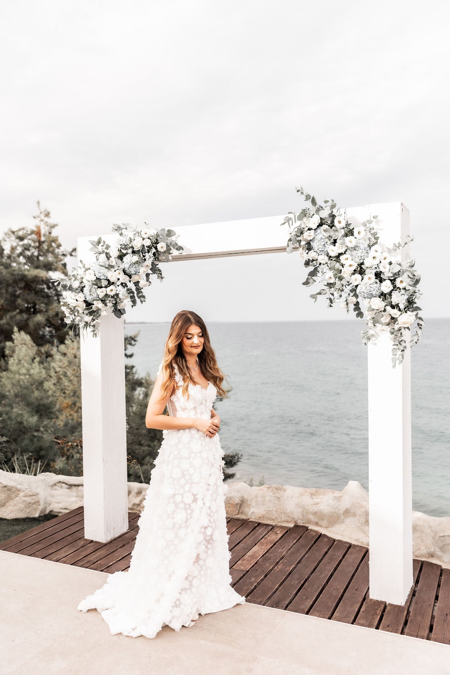 Bridal portraits on a wooden deck overlooking the ocean with white floral decorations.