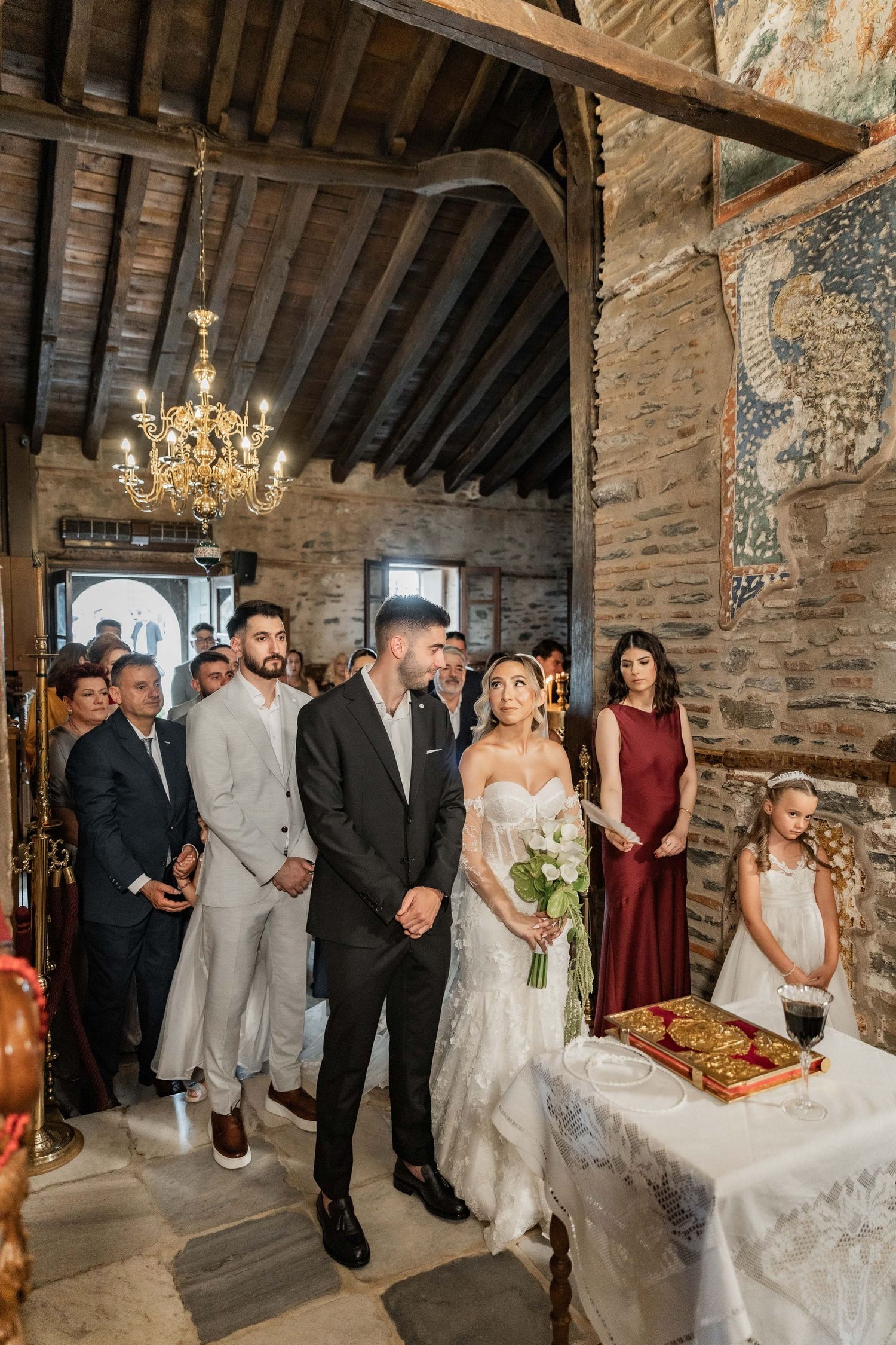 Bride and groom stand at altar in rustic stone chapel surrounded by wedding guests during traditional ceremony.