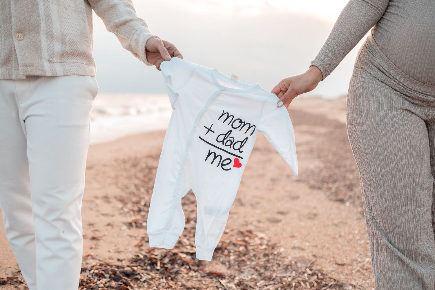 Family wearing coordinated white and beige outfits holds hands while walking on a sandy beach at sunset.