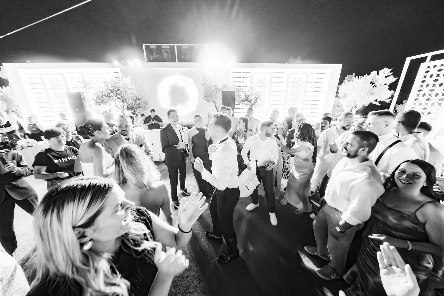Black and white photo of wedding guests dancing and celebrating on a crowded dance floor.